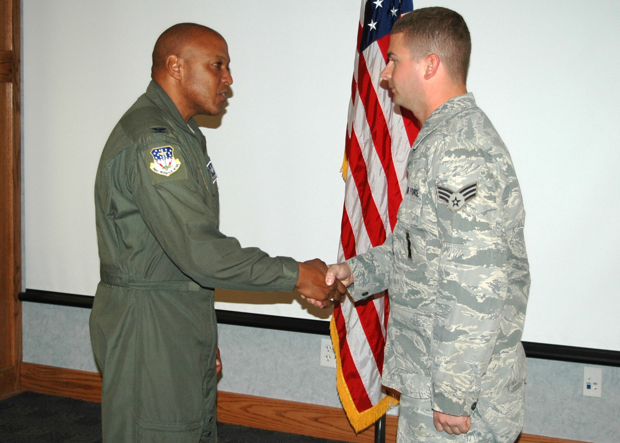 Col. Anthony Cotton, 341st Missile Wing commander, coins Senior Airman  James Hilderbrand, 341st Missile Maintenance Squadron topside technician, prior to a maintenance briefing in the wing conference room Oct. 9. The coin was given to Airman Hilderbrand after successfully completing 100 incident-free missions to Malmstrom's missile complex behind the wheel of a payload transporter. (U.S. Air Force photo/Staff Sgt. Dillon White)