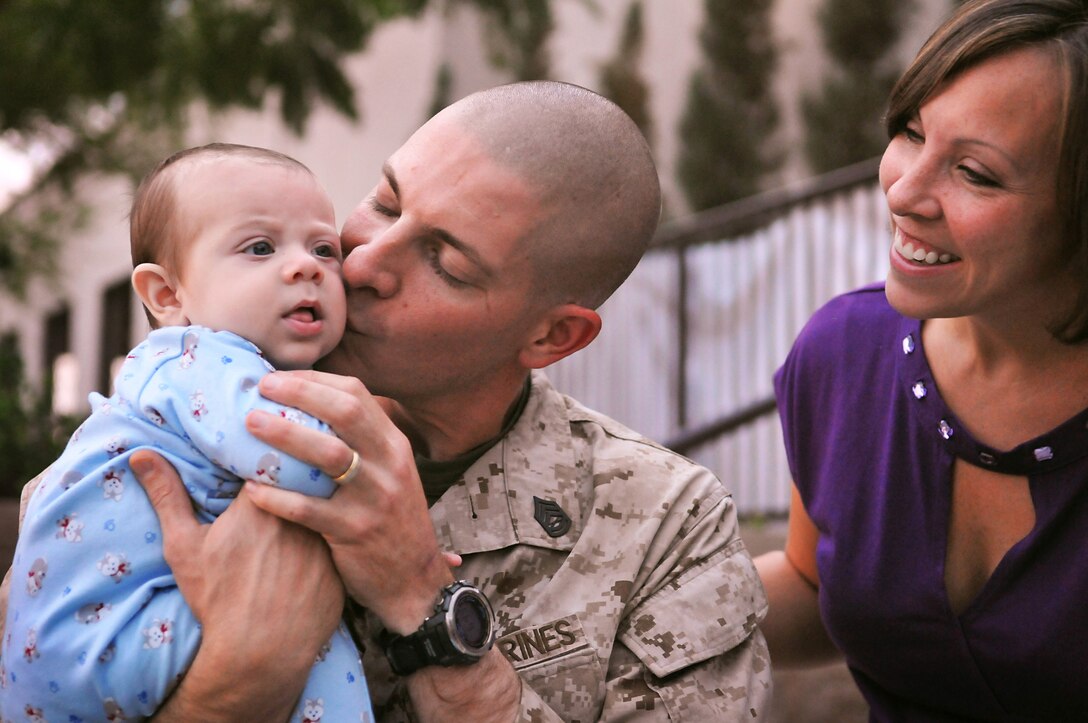 While his wife Jaime looks on, Gunnery Sgt. Tim Clark kisses his infant son Ethan shortly after seeing him for the first time Oct. 15, 2010, when he and 78 other personnel from Marine Air Control Squadron 1 returned home to the Marine Corps Air Station in Yuma, Ariz., from a more than six month deployment to Afghanistan. Ethan was born in June, while his father served as the senior air director for the squadron's tactical air operations center, which managed airspace in southern Afghanistan for approximately 50,000 flights in seven months. "It's very good to finally meet this little guy," said Clark, who also has a 4-year-old daughter Payton. Both Tim and Jaime are natives of Birmingham, Ala.