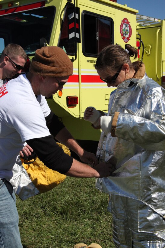 Sgt. Lance C. Risley, left, helps Yaliya Shubina try on equipment worn by aircraft rescue firefighters. The Marines took part in the festivities at Havelock’s 29th annual Chili Festival at Walter B. Jones Park in Havelock this past weekend to help raise awareness about the air station.