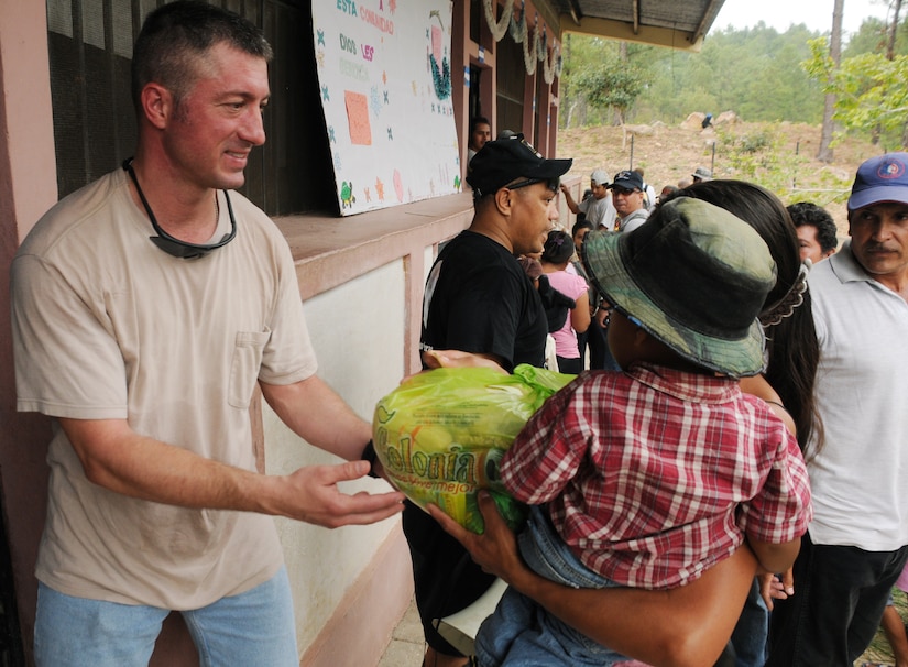 SAN JERONIMO, Honduras --  Greeting a woman and her child, Capt. John Stamm, with Joint Task Forc-Bravo, hands off a bag of food and other supplies during the Chapel Hike here Oct. 16. The Soto Cano Air Base Friendship Chapel sponsors monthly hiking trips that partners JTF-Bravo members with local community leaders, city hall officials and the World Food Program to provide support to surrounding villages in need of food and supplies. (U.S. Air Force photo/Tech. Sgt. Benjamin Rojek)