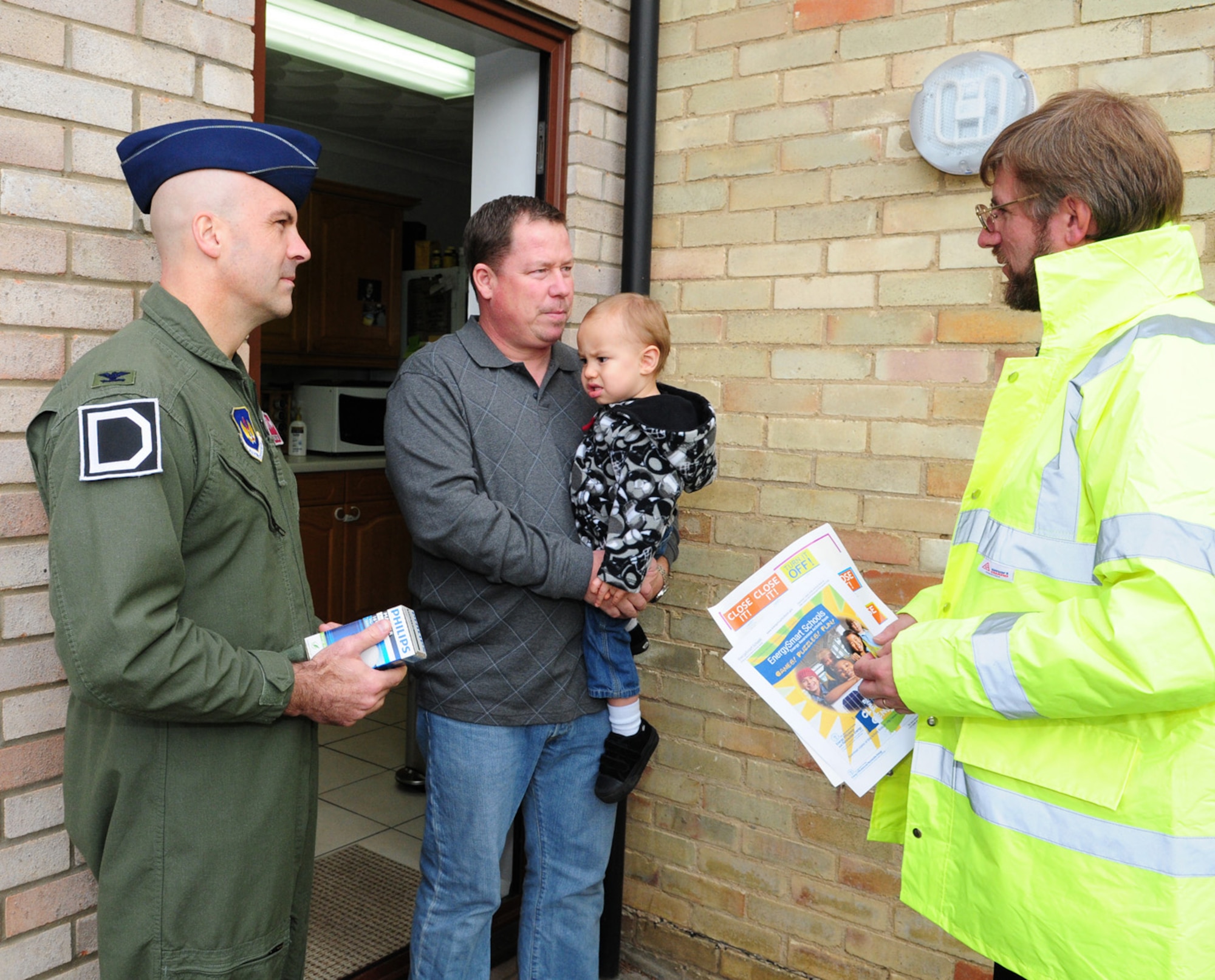 RAF MILDENHALL, England -- Steve Perry, RAF Mildenhall base energy manager, (right) chats with Simon Cooke, dependent of an RAF Lakenheath member, and son Michael, 20 months, before Col. Chad Manske, (left) 100th Air Refueling Wing commander, presents him with a free energy-saving lightbulb as part of Energy Awareness Month Oct. 15. The 100th Civil Engineer Squadron is providing energy- efficient lightbulbs to all those who live in base housing on RAF Mildenhall. (U.S. Air Force photo/Karen Abeyasekere)