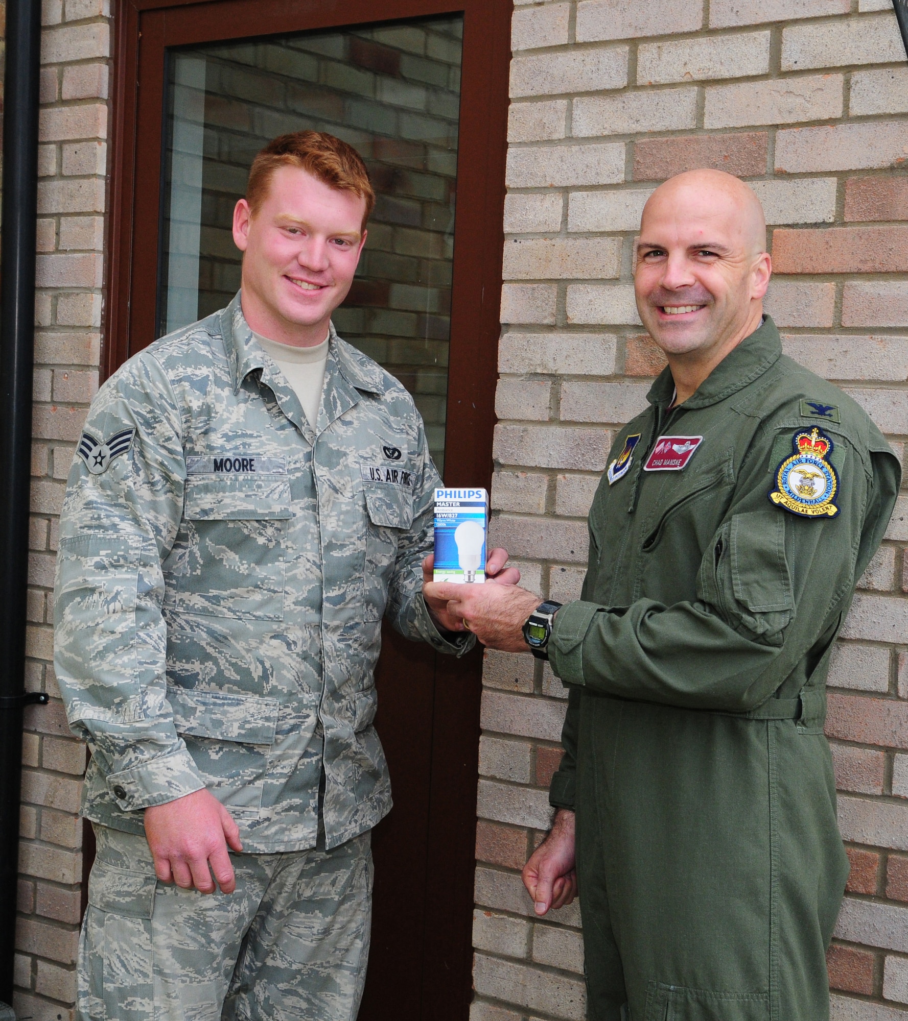 RAF MILDENHALL, England -- Col. Chad Manske, 100th Air Refueling Wing commander, presents Senior Airman Richard Moore, 100th Civil Engineer Squadron, with an energy efficient lightbulb Oct. 15, as part of Energy Awareness Month. To encourage energy conservation, the 100th CES is providing a free lightbulb to military members living in on-base housing. To show his support of this, Colonel Manske visited RAF Mildenhall housing and helped give out some of the energy-efficient lightbulbs. (U.S. Air Force photo/Karen Abeyasekere)