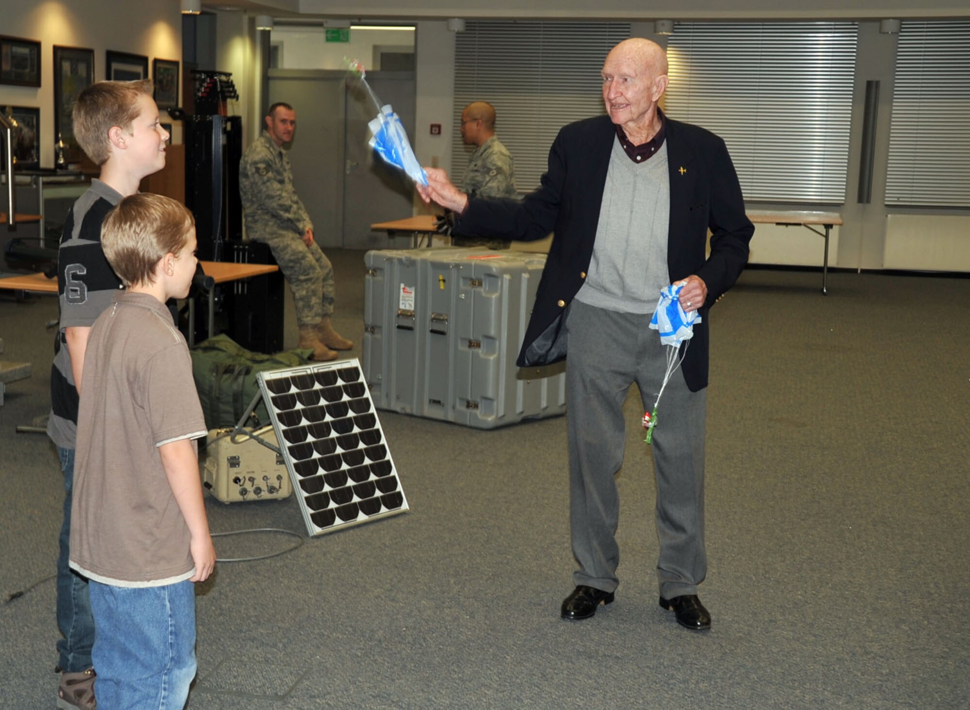 Col. Gail Halvorsen (Ret.) helps two children test their parachutes with toy soldiers holding candy bars.  The soldiers were part of decorations created by the 435th Contingency Response Group at Ramstein Air Base, Germany.  After briefing him on their mission, the group surprised the WWII veteran with a cake celebrating his 90th birthday.  The Berlin Airlift veteran is known for his role in strengthening U.S.-German ties after a goodwill gesture of air dropping candy bars to children in East Berlin turned into a full-scale operation that ended in more than 20 tons of candy delivered via small parachutes.  He is touring Europe and Southwest Asia this week to visit and encourage service members. (U.S. Air Force photo/1st Lt. Kathleen Ferrero)