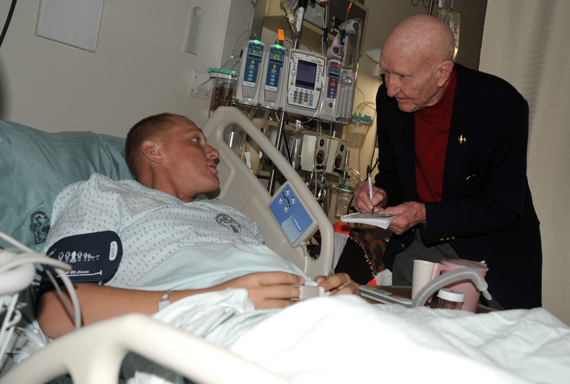 Col. Gail Halvorsen, a retired Air Force colonel known as the Berlin Airlift "Candy Bomber," talks to a U.S. Marine, Lance Cpl. Drake Bies, at Landstuhl Regional Medical Center in Germany.  Colonel Halvorsen recorded contact information for loved ones of the warriors whom he met at the hospital.  The airlift icon is touring Europe and Southwest Asia this week to encourage servicemembers and learn about the evolution of his heritage. (U.S. Air Force photo/1st Lt. Kathleen Ferrero)