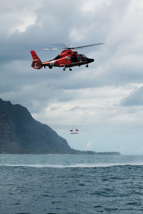 Coast Guard Petty Officer 3rd Class Lopaka Helepololei, a Eurocopter HH-65 Dolphin helicopter flight mechanic, lowers a rescue basket to simulated casualty Cpl. Brad Rosati, a navigation aids technician with Air Traffic Control maintenance, Marine Corps Air Station Kaneohe Bay, during a joint-service aircraft mishap drill over Kaneohe Bay, Hawaii, Oct. 18, 2010. The drill simulated a CH-53D Sea Stallion helicopter crash over water, and allowed the joint-service team to exercise standard operating procedures for air and waterborne rescue operations.