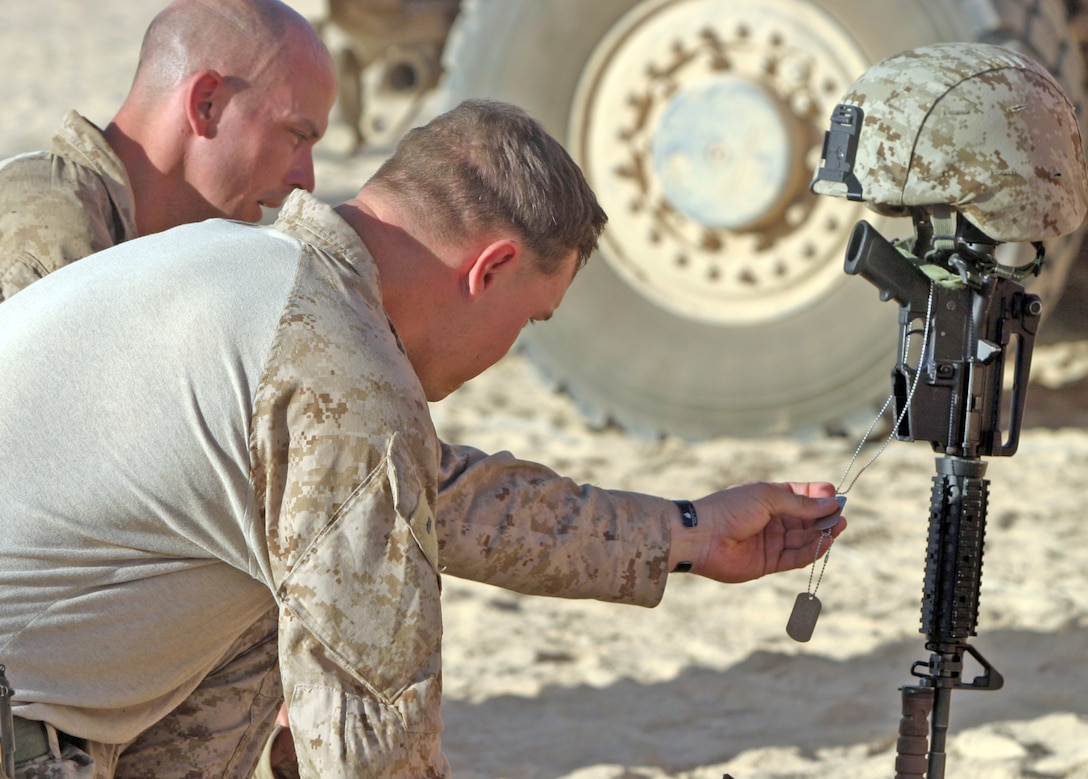 1st Lt. Jason N. Deane, officer in charge of non-kinetic operations with Weapons Company, 2nd Battalion, 9th Marine Regiment, holds the identification-tags of Sgt. Frank R. Zaehringer, an anti-tank missile-man with Weapons Company, 2/9, off a battlefield memorial cross rifle display honoring his life during a memorial service at Forward Operating Base Camp Hanson, Helmand Province, Afghanistan. Zaehringer’s life was tragically ended Oct. 11, while conducting combat operations in Northern Marjah.