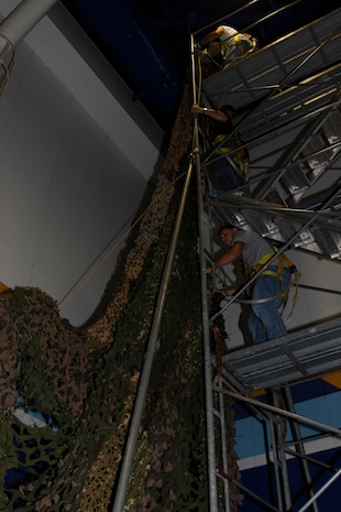 Marines work together to hang hundreds of feet of camouflage netting to the IronWorks Gym sports court wall here for the Marine Corps Birthday Ball, Oct. 20. Forty-one Marines from around the station were responsible for turning the gym’s sports courts into a venue fit to celebrate the 235th birthday of the Marine Corps.