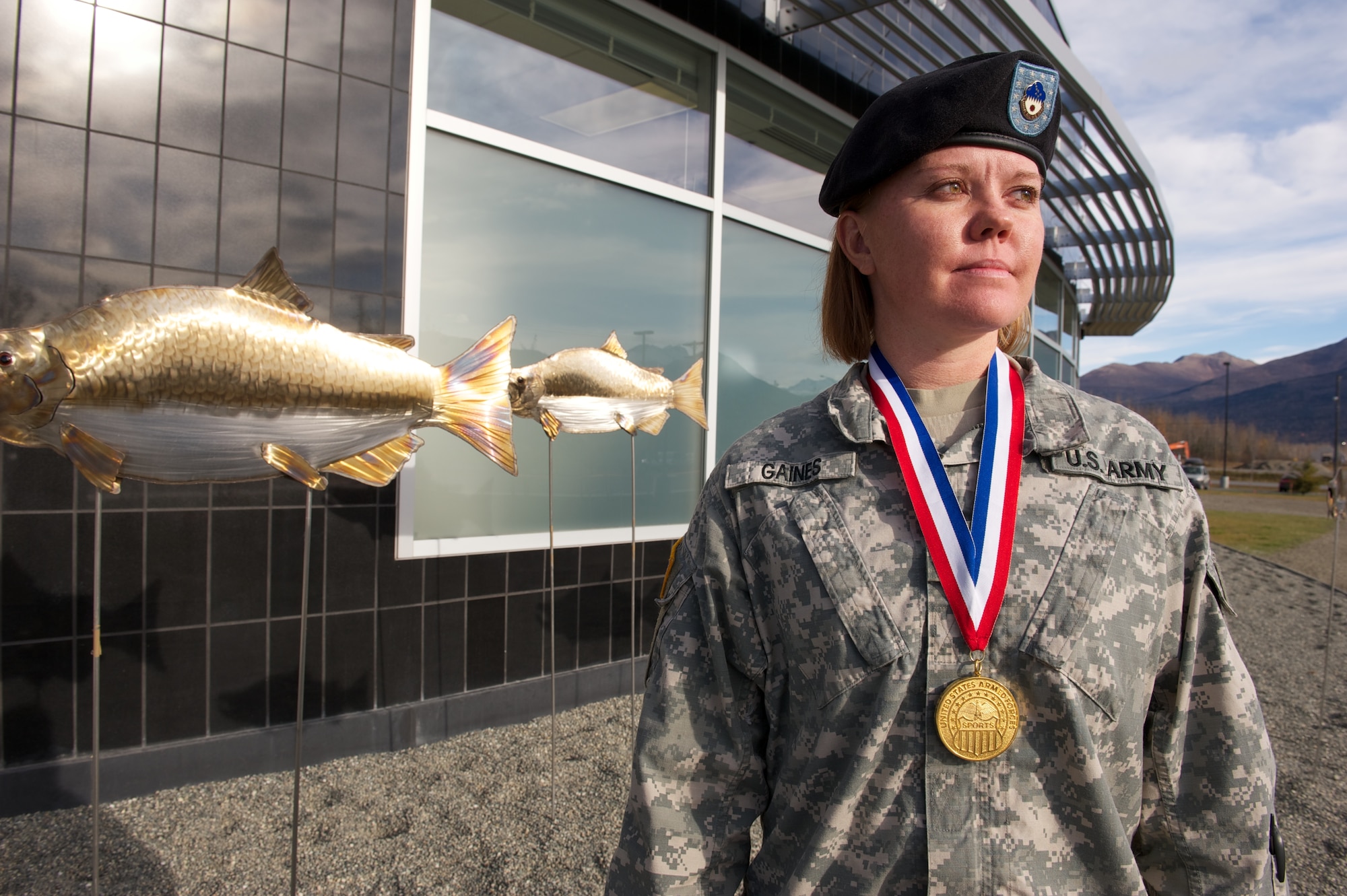 Army Sgt. Margaret Gaines, Medical Department Activity-Alaska, wears her 2010 Armed Forces Women’s Softball Championship gold medal, Oct. 8, in front of a salmon motif at the Troop Health Clinic. (U.S. Air Force photo/David Bedard)