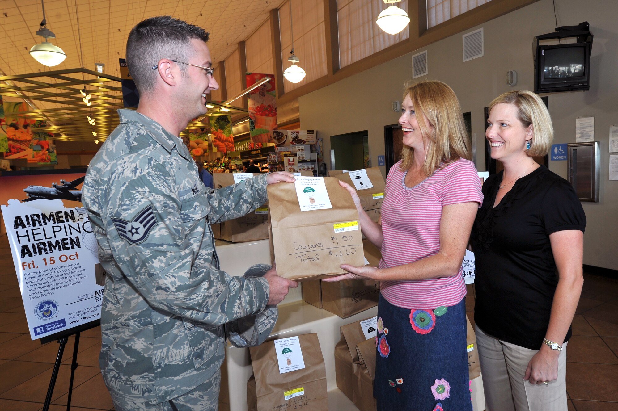 Staff Sgt. Tim McGee, 19th Medical Group dental lab technician, receives an Airmen Helping Airmen food pantry bag Oct. 15 from Ashley Minihan (center), wife of Col. Mike Minihan, 19th Airlift Wing commander; and Susan Czelusta, wife of Col. Mark Czelusta, 314th Airlift Wing commander, at the commissary. Airmen Helping Airmen is a new program to help Team Little Rock families in need.  (U.S. Air Force photo by Staff Sgt. Chris Willis)