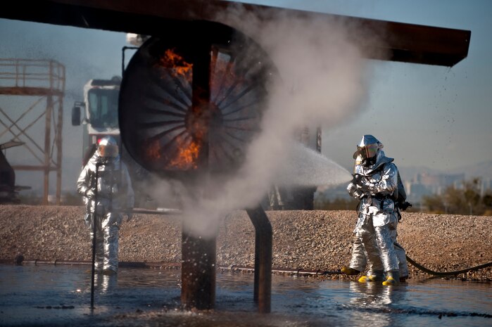 NELLIS AIR FORCE BASE, Nev. --  Brig. Gen. David Thompson, U.S Air Force Warfare Center vice commander, works with Senior Airman Nathan Aguilera and Senior Airman Michael Nieman, 99th Civil Engineer Squadron Fire Department firefighters, on the proper use of the buddy system while fighting a simulated aircraft fire at the Nellis live-fire training facility Oct. 18. The 99th Civil Engineer Squadron and fire emergency services flight invited Nellis senior leaders to a live-fire aircraft and structural exercise so they could experience some of the challenges firefighters encounter during real-world situations. (U.S. Air Force photo by Tech. Sgt. Michael R. Holzworth)(Released)