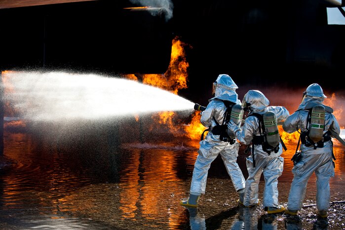 NELLIS AIR FORCE BASE, Nev. --  Brig. Gen. David Thompson, U.S Air Force Warfare Center vice commander, assists Senior Airman Nathan Aguilera and Senior Airman Michael Nieman, 99th Civil Engineer Squadron Fire Department firefighters, demonstrate the proper use of the buddy system while fighting a simulated aircraft fire at the Nellis live fire training facility Oct. 18. The 99th Civil Engineer Squadron and fire emergency services flight invited Nellis senior leaders to a live-fire aircraft and structural exercise so they could experience some of the challenges firefighters encounter during real-world situations. (U.S. Air Force photo by Tech. Sgt. Michael R. Holzworth)(Released)