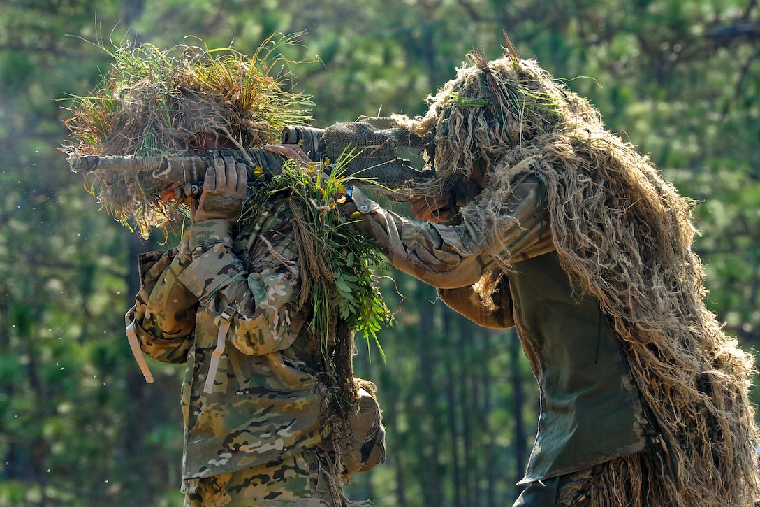 Two snipers wearing ghillie suits combine to form an over-the-shoulder firing position during competitive shooting at the 10th Annual International Sniper Competition on Fort Benning, Ga., Oct. 14, 2010. A ghillie suit is a type of camouflage from cloth or fibers, with the name originating from gille, the Gaelic word for servant.