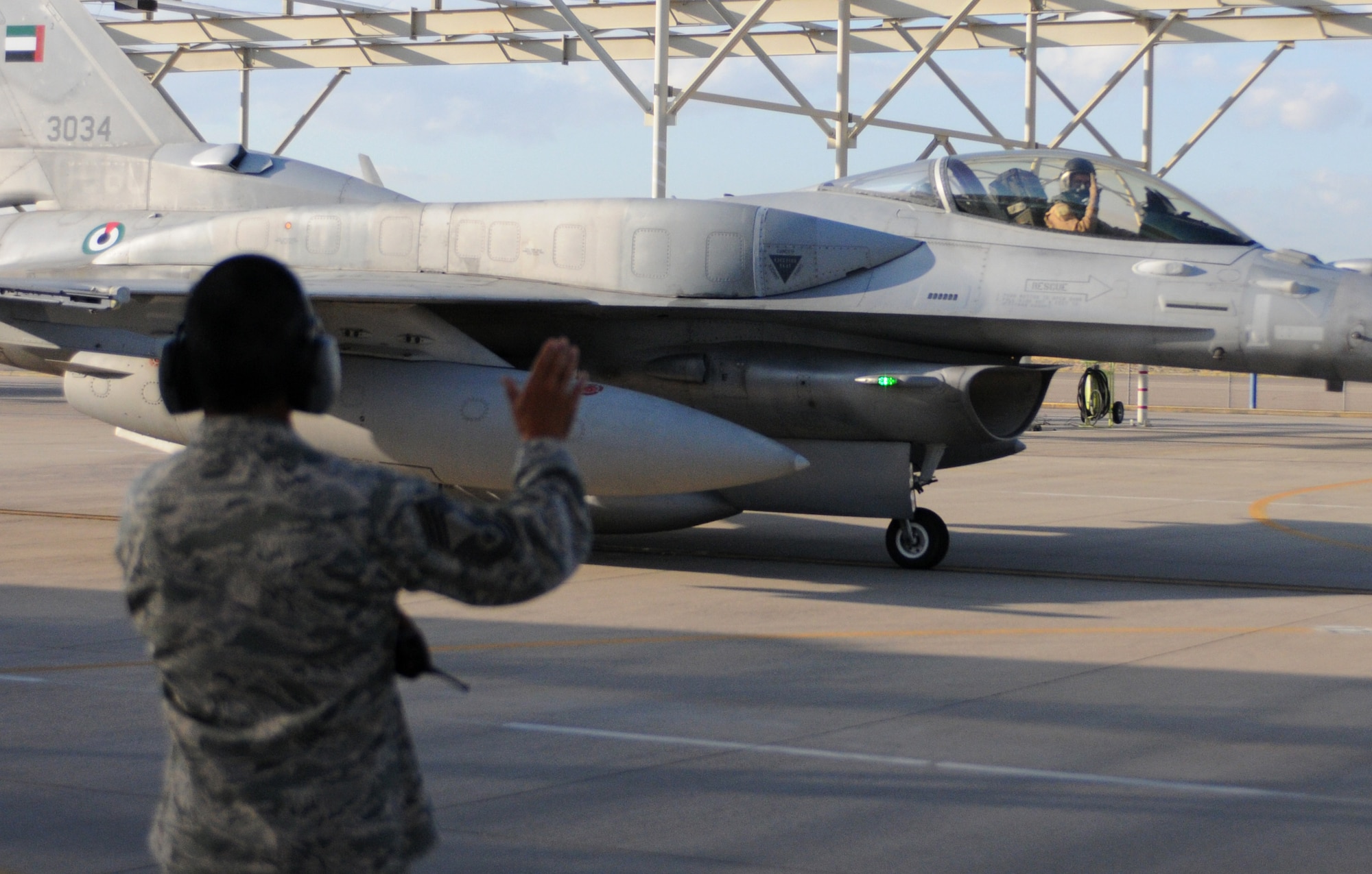 Chief Master Sgt. Vic Mendoza, maintenance supervisor for the F-16 Block 60 program in Tucson, waves goodbye as one of his aircraft departs for the United Arab Emirates. Five UAE-owned F-16s took off Oct. 20 with 600 gallon fuel tanks on their wings for the long flight home. (US Air Force photo/Maj. Gabe Johnson)