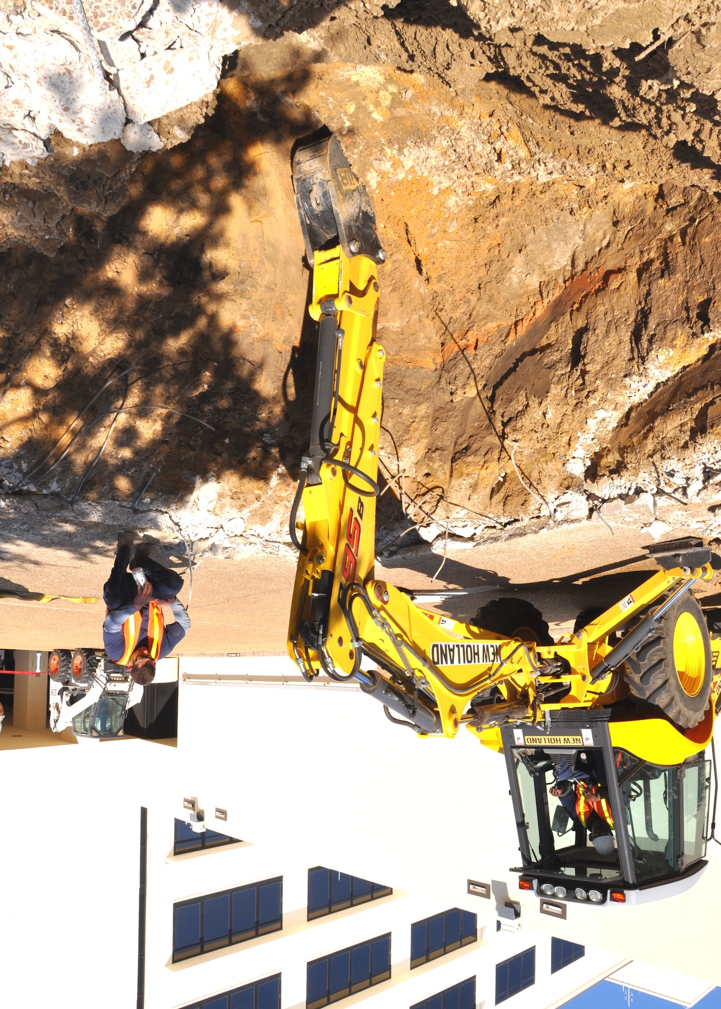 Thomas Walker operates a backhoe while Ryan Callagy guides him as they excavate the 81st Medical Group Hospital’s “A” tower ramp to locate the 8-inch water main that
ruptured early Oct. 8. Don Kinman, CSC civil engineer manager, estimates the pipe may have been 50-60 years old. The line, buried between 15 and 18 feet under the
ramp, is one of three serving the hospital so the facility was not without water while the pipe was being repaired. CSC completed repairs Oct. 9, but the ramp remains closed until the roadway is repaired. Mr. Walker and Mr. Callagy are from CSC civil engineering equipment operations.  (U.S. Air Force photo by Steve Pivnick)
