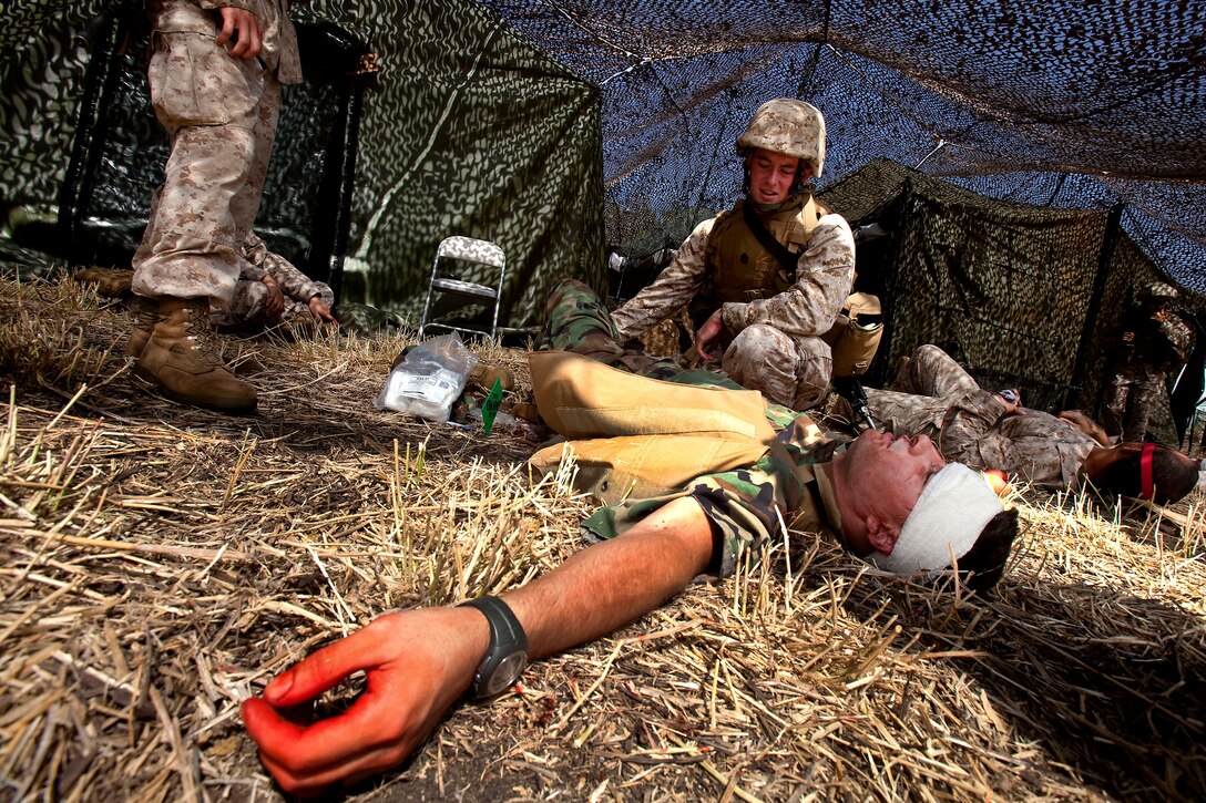 Gunnery Sgt. Joseph Maupai, training and operations chief, 3rd Radio Battalion, assesses the injuries of simulated casualty Seaman Brad Parkerson, a corpsman with 21st Dental Company, during a mass casualty evacuation drill at Dillingham Air Field in Mokuleia, Hawaii, Oct. 21. Moulage kits attached to the casualties’ rubber wounds poured out fake blood, forcing the Marines to properly secure dressings, bandages, tourniquets, and apply pressure before the blood from the wounds would clot.