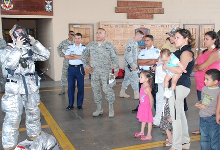 SOTO CANO AIR BASE, Honduras --  A 612th Air Base Squadron firefighter (left) demonstrates putting on a protective fire suit as part of a tour of the fire department during Foreign Service National Family Day here Oct. 22. FSNs and their family members also visited the 1-228th Aviation Regiment and the Honduran Air Force Academy, among other places on Soto Cano. (U.S. Air Force photo/Capt. John Stamm)