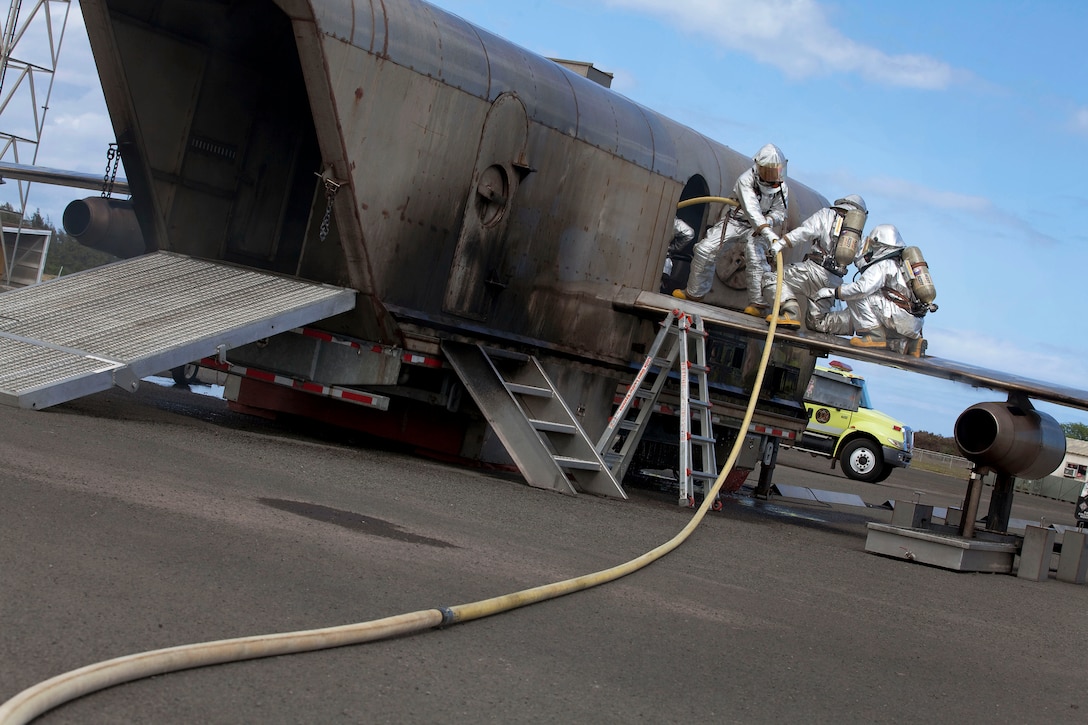 As a fire simmers inside the Mobile Aircraft Firefighting Training Device, firefighters with Aircraft Rescue Firefighting, Marine Corps Air Station Kaneohe Bay, work to pull in the hose toward the turret operator during burn training near the MCAS flight line, Oct. 24, 2010. The turret operator is the firefighter who puts out the most water on the fire, said Cpl. Brice Kuehn, rescue man, ARFF.