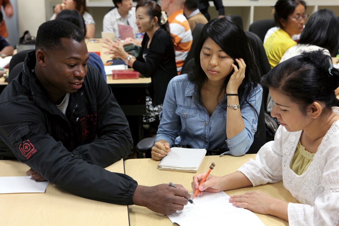 Cpl. Cedric Littleton, a hazardous material noncommissioned officer with Headquarters Battalion, 3rd Marine Division, III Marine Expeditionary Force, assists Harumi Shimabukuro, right, a first-time student, with a written translation during a weekly English class held at the Education Center Oct. 25.