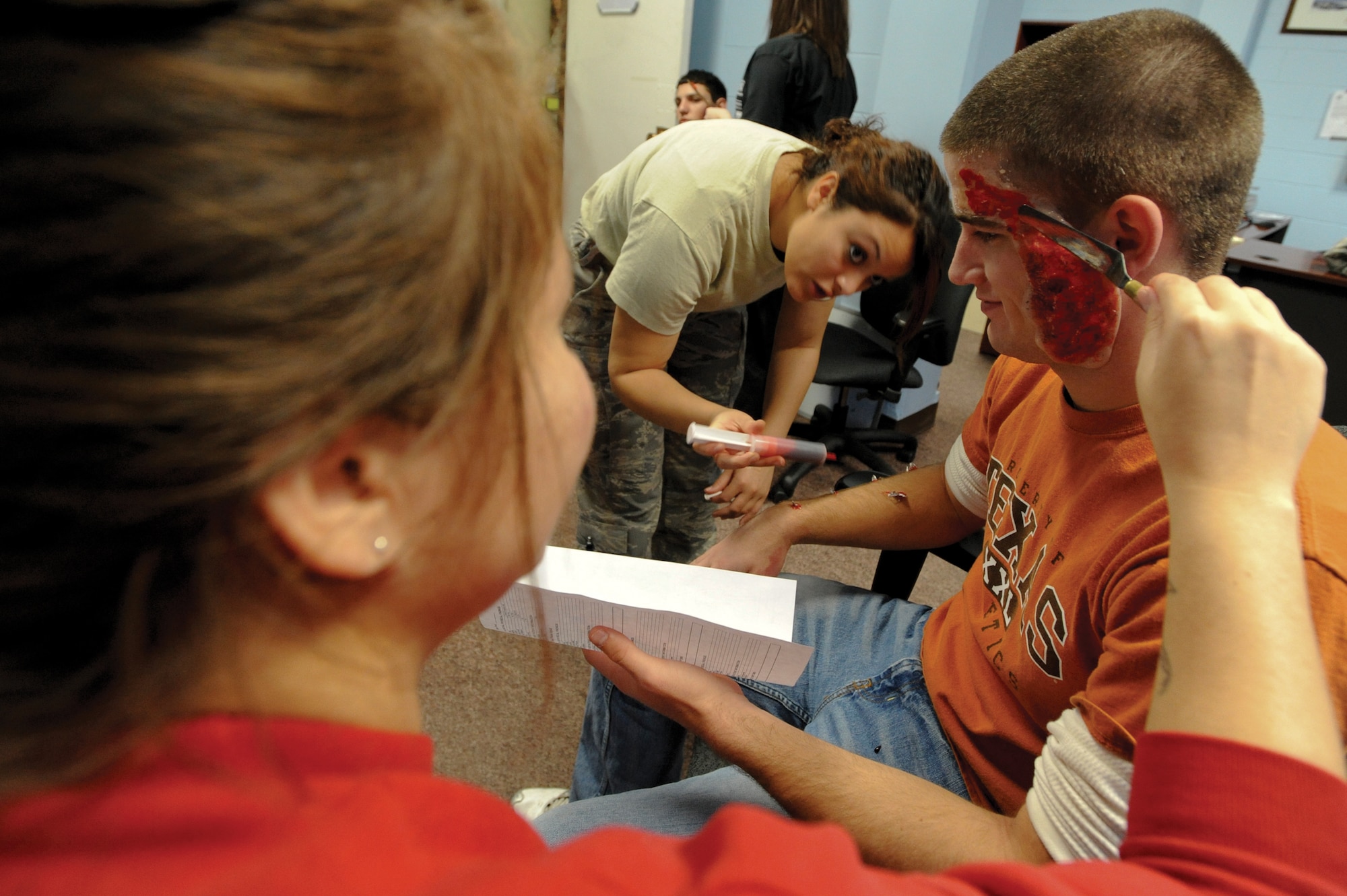 Ashley McCoy, moulage artist, applies a face wound as Airman 1st Class Ilyana Luciano, 673d Dental Squadron, applies fake shrapnel to Jacob Seale, an Emergency Management Exercise victim at Joint Base Elmendorf-Richardson, Alaska, October 19. (U.S. Air Force photo/Staff Sgt. Joshua Garcia)