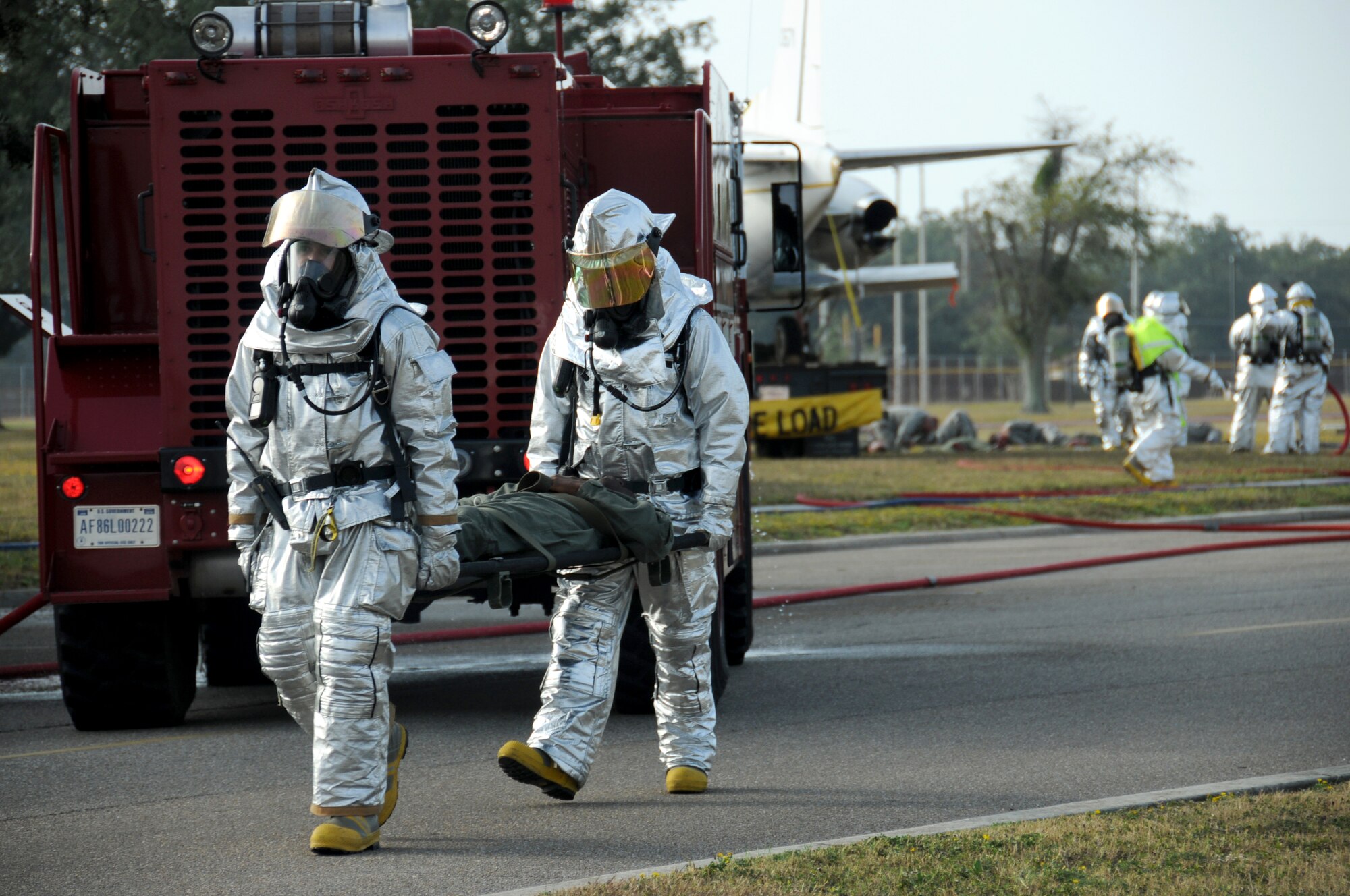 Keesler fire fighters carry a crash victim to the triage area for treatment in Tuesday's major accident response exercise.  During the exercise a C-130J made a hard landing, lost engine power and crashed into a six-passenger van, coming to rest on the Triangle track north of Alho Manor.  The scenario also included a spill from chemicals on the aircraft, hydraulic fluid and JP-8 fuel.  Three people "died" and 30 were "injured" in the accident, part of this week's Air Education and Training Command Compliance Inspection.  (U.S. Air Force photo by Kemberly Groue)