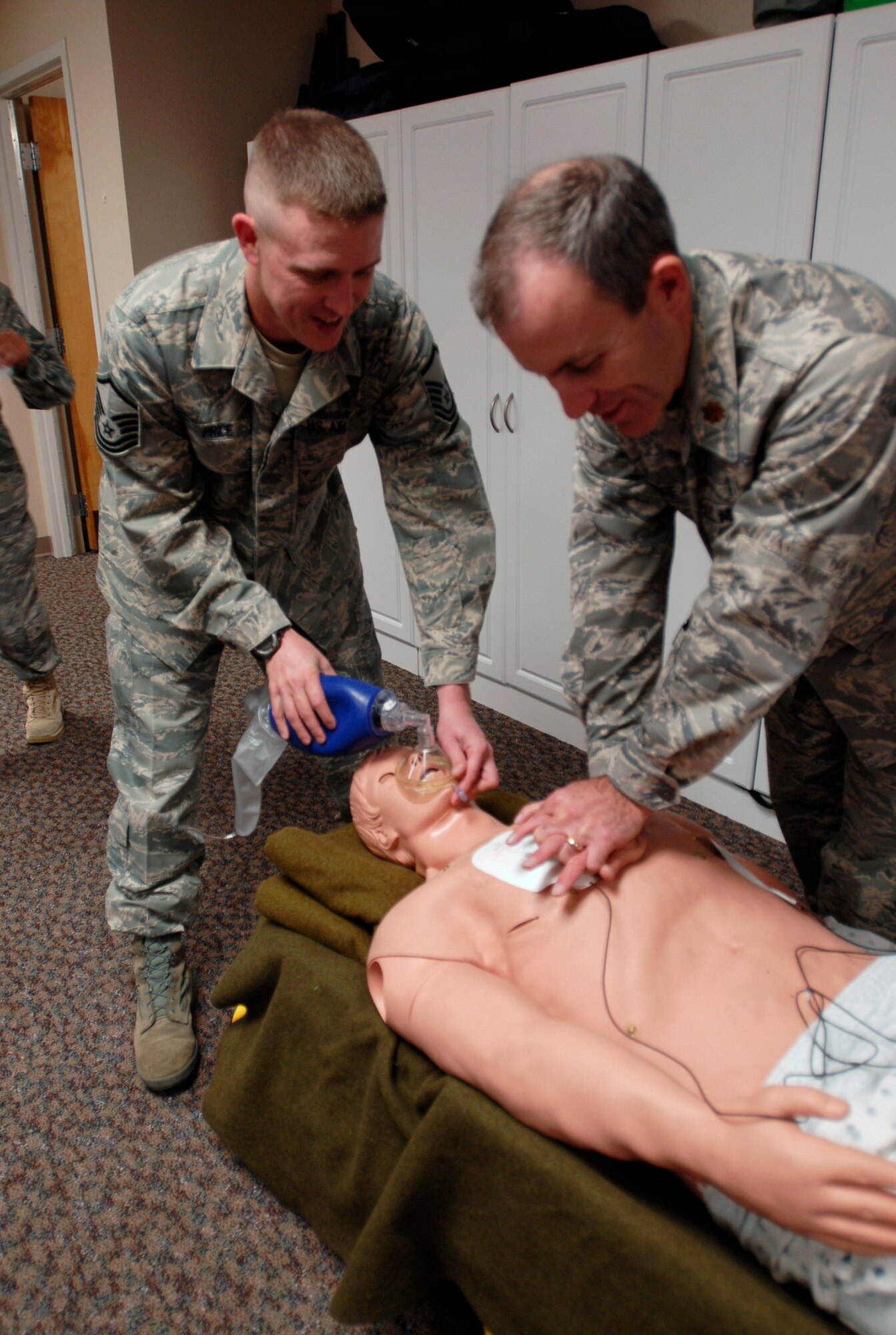 Master Sgt. Michael Price, an aerospace physiology technician with the 21st Aerospace Medicine Squadron, and Maj. Gary Rice, flight commander for the 21 AMDS/Aerospace and Operational   Physiology Unit, practice chest compressions and breaths on a life-size Medi-Man dummy. The mannequin simulates a person's vital statistics and movement to help individuals understand what performing CPR on a real person would be like. (U.S. Air Force photo/Airman 1st Class Jessica Hines)
