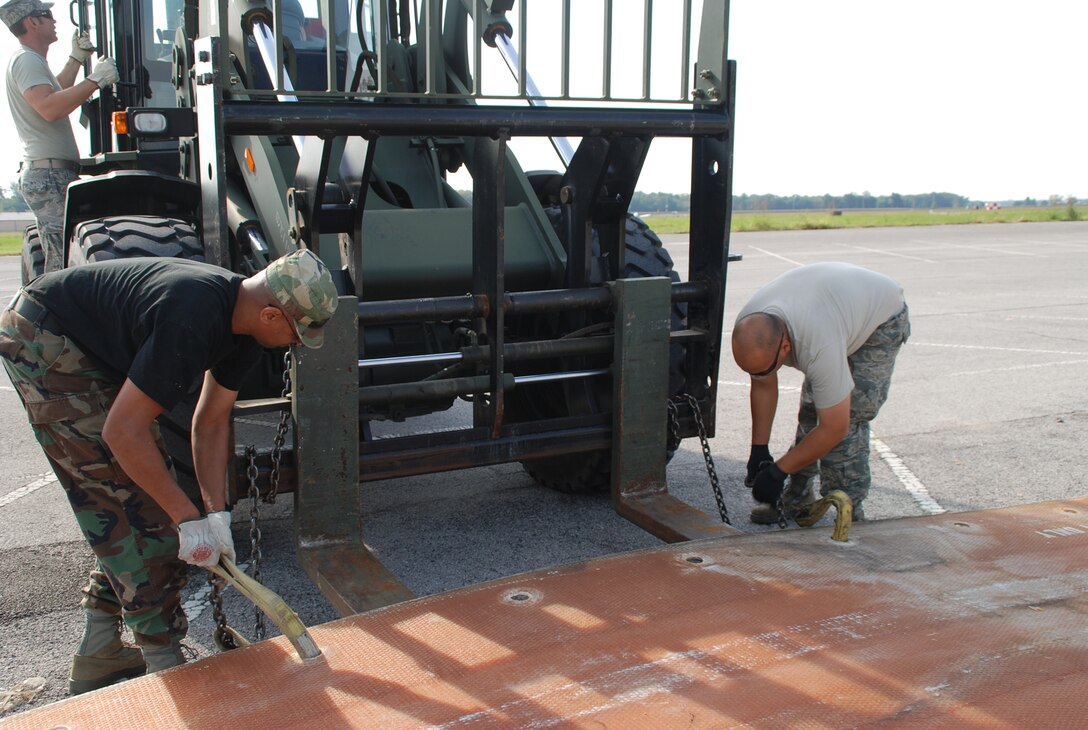 932nd Airlift Wing Civil Engineering Squadron members attach straps and chains in
preparation to stretch a mat to line up with a second mat used to cover a simulated crater.  The fold-out, fiberglass mats can be quickly deployed over craters and large holes, keeping the runway usable for aircraft.  (U.S. Air Force photo/Tech. Sgt. Dan Oliver)