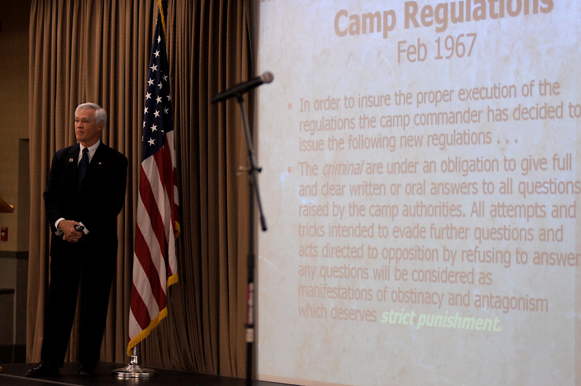 Retired Lt. Col. Barry Bridger, North Vietnam Prisoner of War survivor, stands proudly next to the Camp Regulations that were posted on the prison wall he was in for six years at Hanoi Hilton Prison Camp during his speech Oct. 27 at the Northern Lights Club on Grand Forks AFB.  Colonel Bridger was in the Grand Forks area sharing his POW story with the local community; he also travels around the world sharing his experience. (U.S. Air Force photo by Senior Airman Amanda N. Stencil)