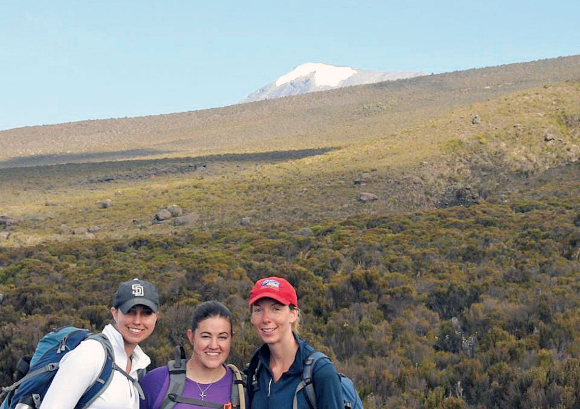 Maj. Lisa Reaver (center) poses with fellow climbers Lauren Drietzler (left) and Heather Ruhle after summiting Mount Kilimanjaro’s Uhuru Peak, visible in the background. (Courtesy photo)