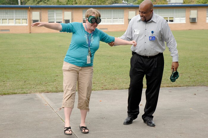 Mr. Selwyn Stephens helps Mrs. Leah Batiz as she tries to walk while wearing drunk goggles during a demonstration held by members of Joint Base Charleston at Lambs Elementary Oct. 26, 2010 as part of Red Ribbon Week. Members of JB CHS visited local elementary schools during the week long campaign to raise public awareness and mobilize communities to combat tobacco, alcohol and drug use. Mr. Stephens is with the 628th Medical Group as the drug demand reduction program manager. Mrs. Batiz is a 5th grade teacher at Lambs Elementary. (U.S. Air Force photo/Staff Sgt. Marie Brown)