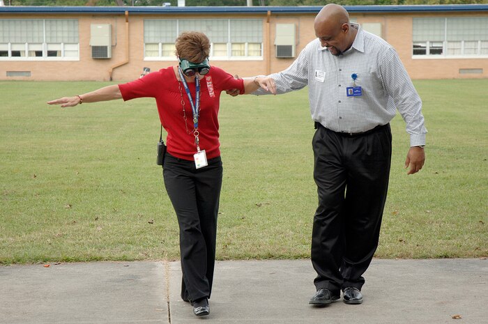 Mr. Selwyn Stephens helps Mrs. Amy Peake as she tries to walk while wearing the drunk goggles during a demonstration held by members of Joint Base Charleston at Lambs Elementary Oct. 26, 2010 as part of Red Ribbon Week. Members of Joint Base Charleston visited local elementary schools during the week-long campaign to raise public awareness and mobilize communities to combat tobacco, alcohol and drug use. Mr. Stephens is with the 628th Medical Group as the drug demand reduction program manager. Mrs. Peake is a 4th grade teacher at Lambs Elementary. (U.S. Air Force photo/Staff Sgt. Marie Brown)
