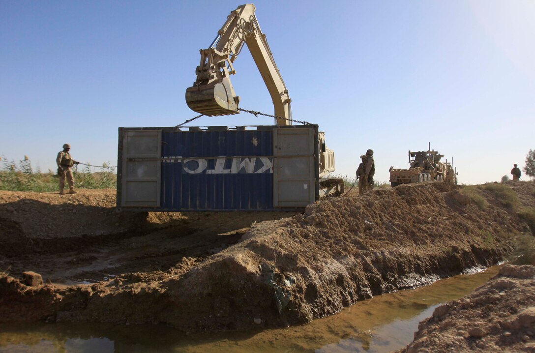 Marines with Engineer Company, Combat Logistics Battalion 3, 1st Marine Logistics Group (Forward), construct a bridge in Trakh Nawa, Afghanistan, Oct. 27. In order to make the bridge more permanent, the Marines packed soil onto a metal storage container.