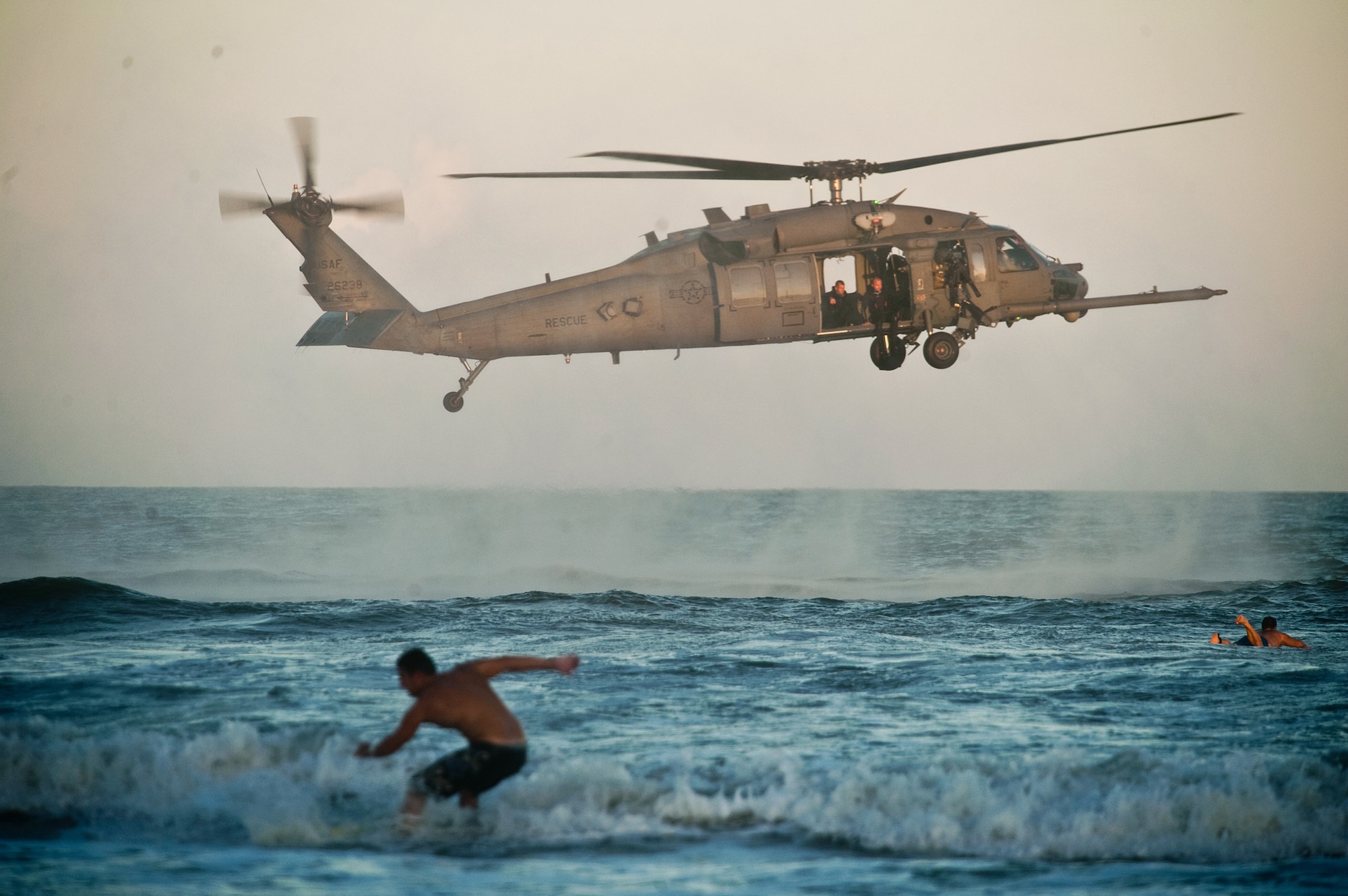 Surfer catch the waves as pararescuemen in an HH-60G Pave Hawk prepare to descend to the water during a rescue demonstration Oct. 27, 2010, at Cocoa Beach, Fla.  The demonstration was part of Air Force Week Cocoa Beach. The pararescuemen are from the Air Force Reserve Command’s 920th Rescue Wing at Patrick Air Force Base, Fla. (U.S. Air Force photo/Lance Cheung)


