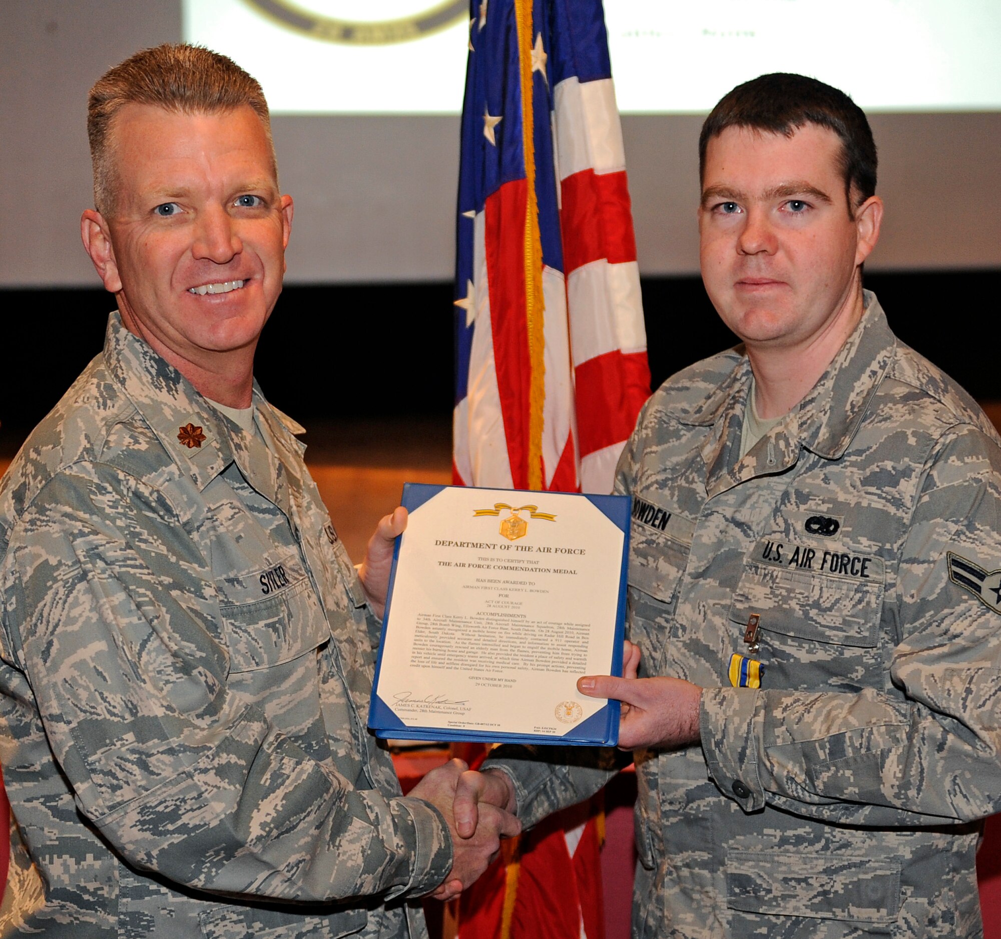 ELLSWORTH AIR FORCE BASE, S.D. – (Right) Airman 1st Class Kerry Bowman, Aircraft Maintenance Squadron aerospace propulsion specialist, is presented the Air Force Commendation Medal by Maj. Brian Sitler, 28th AMXS commander, at the base theater, Oct. 29.  The medal was awarded to Airman Bowman for his act of courage, Aug. 28.  While driving to work, he spotted a burning home, called 911 and rescued an elderly man from the fire. (U.S. Air Force photo/Staff Sgt. Marc I. Lane)