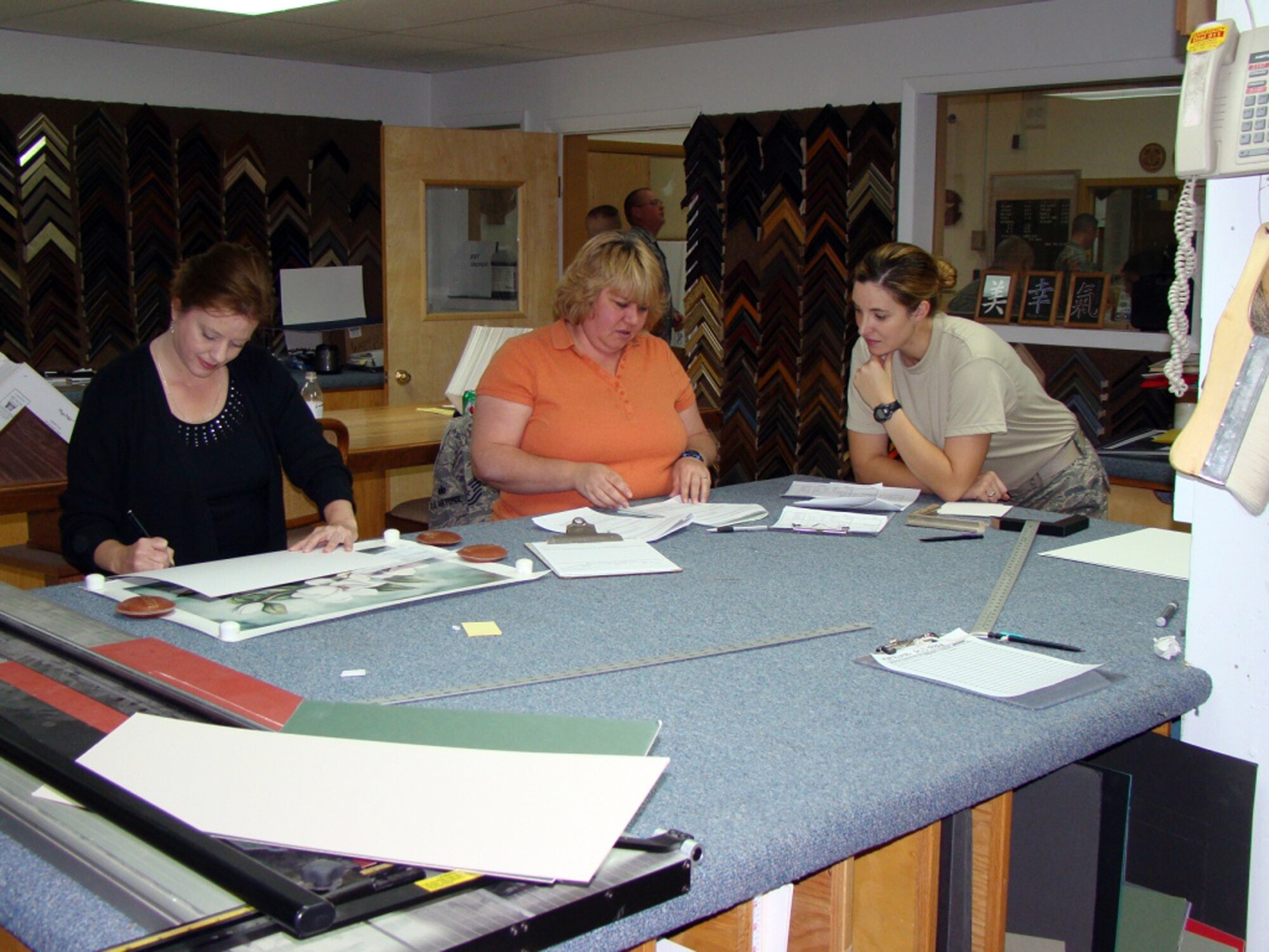 Cheryl Lowe, 90th Forces Support Squadron, shows Tech. Sgt. April Borecki, 90th Missile Security Forces Squadron, and Sandy Chouest, wife of Chaplain Maj. Alan Chouest, 90th Missile Wing Chaplain, how to measure their picture so they can obtain the right framing dimensions during the Squadron Day on Oct. 8. (U.S. Air Force photo by Maj. Joel Briske)