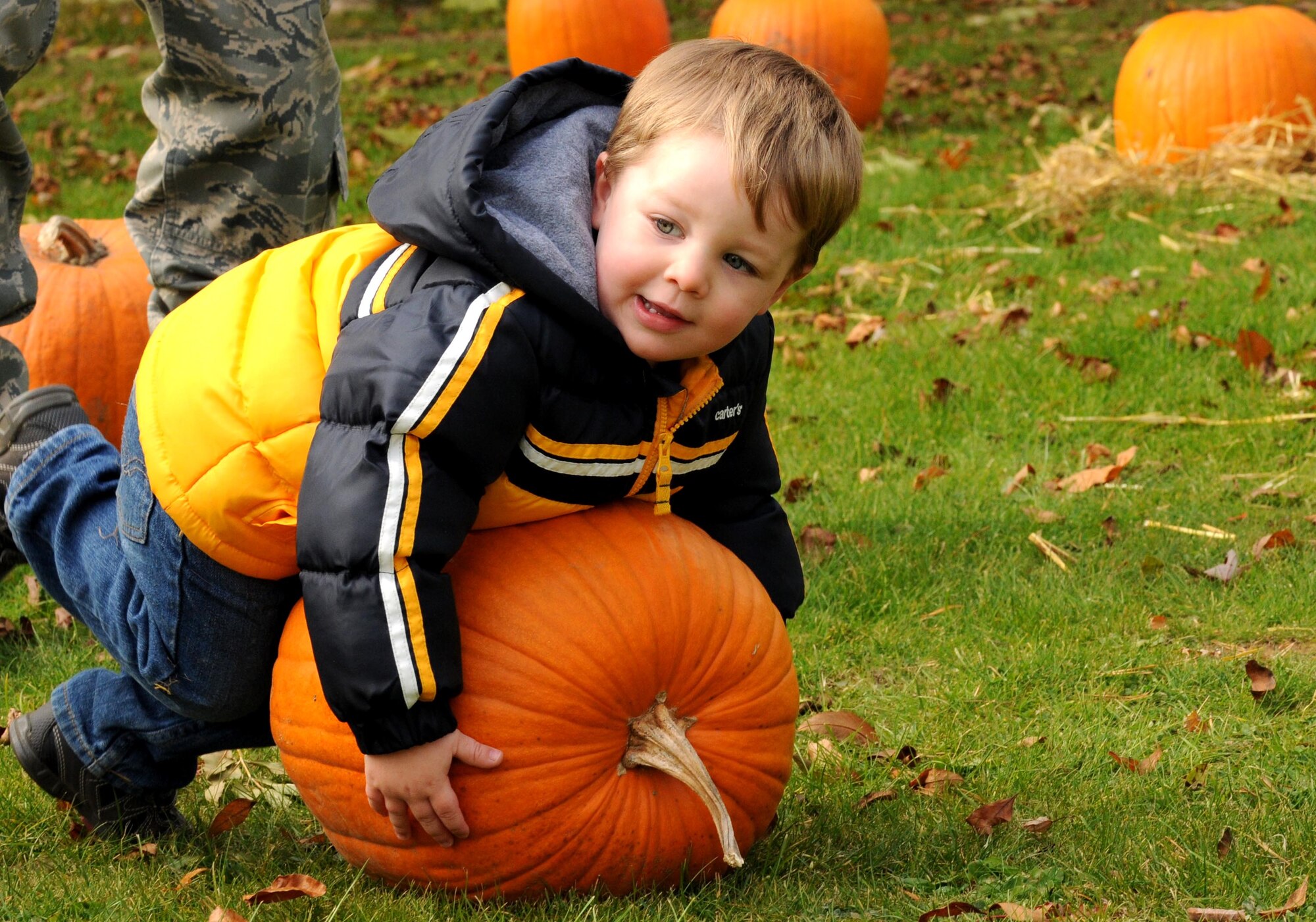 SPANGDAHLEM AIR BASE, Germany – Jayden Phillips, 2, son of Tech. Sgt. Kenneth Phillips, 52nd Aircraft Maintenance Squadron, tries to pick up the pumpkin he picked out for his family Oct. 27. Children from Spangdahlem’s day care and elementary school came to the pumpkin patch to select a pumpkin for their family and have their picture taken. (U.S. Air Force photo/Airman 1st Class Matthew B. Fredericks)