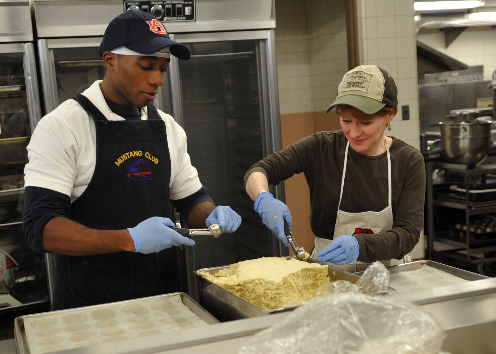 (L-R) Senior Airman Michael Garrett, 731st Air Mobility Squadron, and Robyn Matthews scoop dough onto trays during the annual "Cookie Crunch" at Osan Air Base.  "Cookie Crunch" is sponsored by the Osan Officers' Spouses' Club. More than 80,000 cookies will be baked in the Mustang Club kitchen for all single and unaccompanied military members stationed at Air Force installations in the Republic Of Korea for delivery in mid-December. (U.S. Air Force/Senior Airman Evelyn Chavez)
