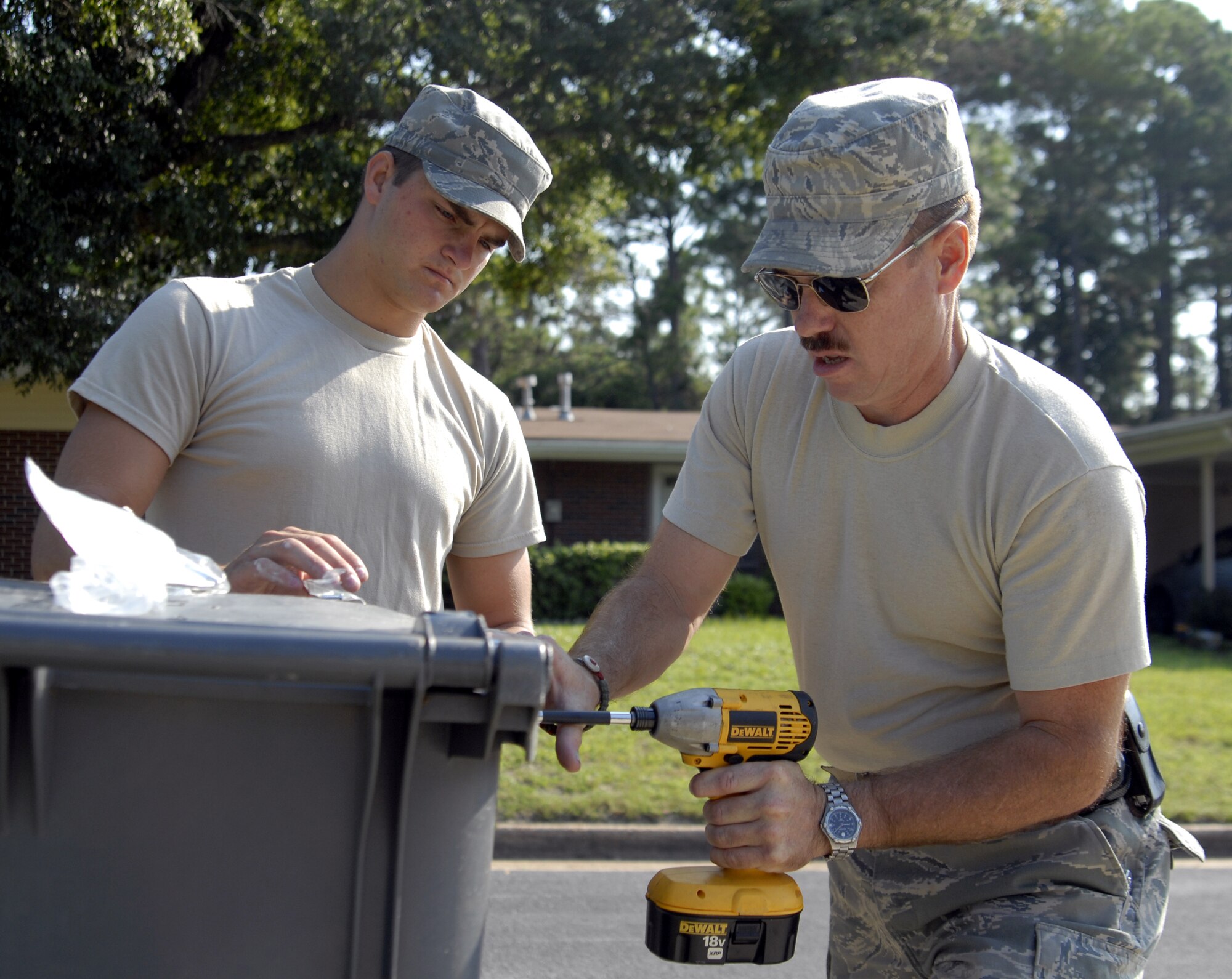 Master Sgt. Lawrence Wood, 1st Special Operations Civil Engineer Squadron heavy equipment superintendent, and Airman Michael Featherston, Hurlburt Field Fire Department, install a new latch on a refuse container in the Pine Shadows housing area at Hurlburt Field, Fla., August 25, 2010. The improved fasteners render the cans bear-resistant the cans in the houses closest to the forest perimeters of the neighborhood and are part of the 1st SOCES’s effort to curb bear activity on base. (DoD photo by U.S. Air Force Airman 1st Class Joe McFadden) (RELEASED)