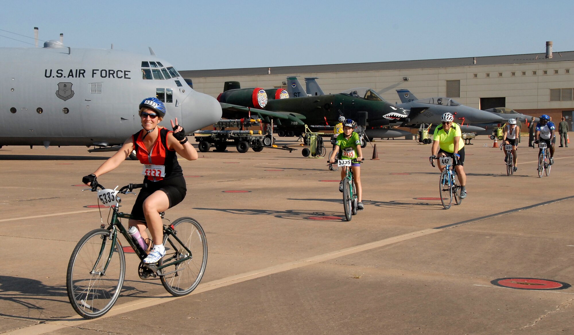 Riders from the Hotter ‘n Hell Hundred race pass through Air Power Alley during their route on Sheppard Air Force Base, Texas, Aug. 28.  Air Power Alley featured a display of Sheppard aircraft lined up for cyclists to view and take photos.  A few of the 80th Flying Training Wing’s student pilots were present and took pictures with cyclists. (U.S. Air Force photo/Mike Litteken)