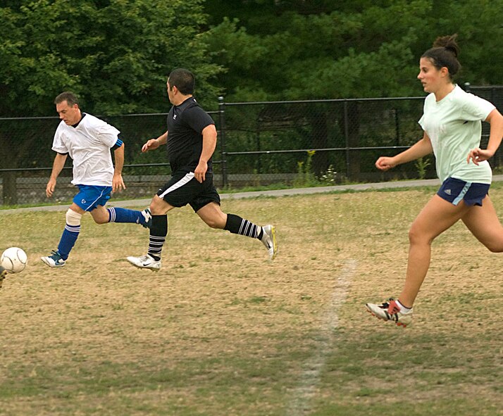 HANSCOM AIR FORCE BASE, Mass. - Dennis Bentley (right) kicks the ball as Capt. Reyn Yamashiro and Cali Rodriguez run close behind during a recent intramural soccer game between Players Pool and 350th/C2ISR. Soccer intramural season was played throughout the summer on the soccer fields next to Memorial Park. (U.S Air Force photo by Walter Santos)