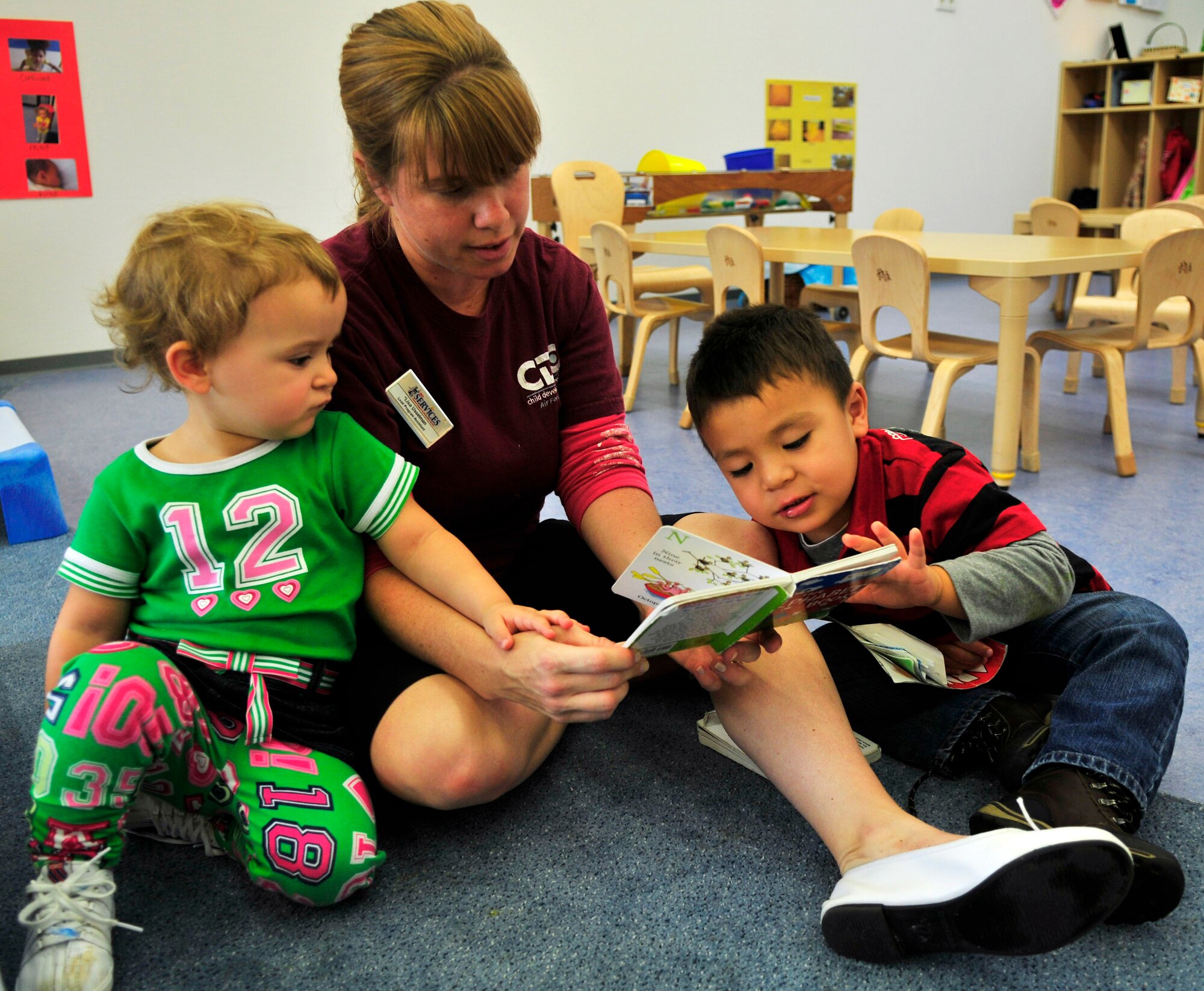 (Left to right) Makenzie Neill, daughter of Tech. Sgt. Adrien and Staff Sgt. Chase Neill, 21st Operational Weather Squadron; Lisa Usselman, Kaiserslautern Military Community Child Development Center lead program assistant in the toddler's room; and Jonathan Figueroa, son of Tech. Sgt. Mario, 786th Civil Engineer Sqadron, and Paulita Figueroa, CDC employee, read together after nap time at the new CDC, Ramstein Air Base, Germany, Sept. 1, 2010. (U.S. Air Force photo by Senior Airman Amanda Dick)