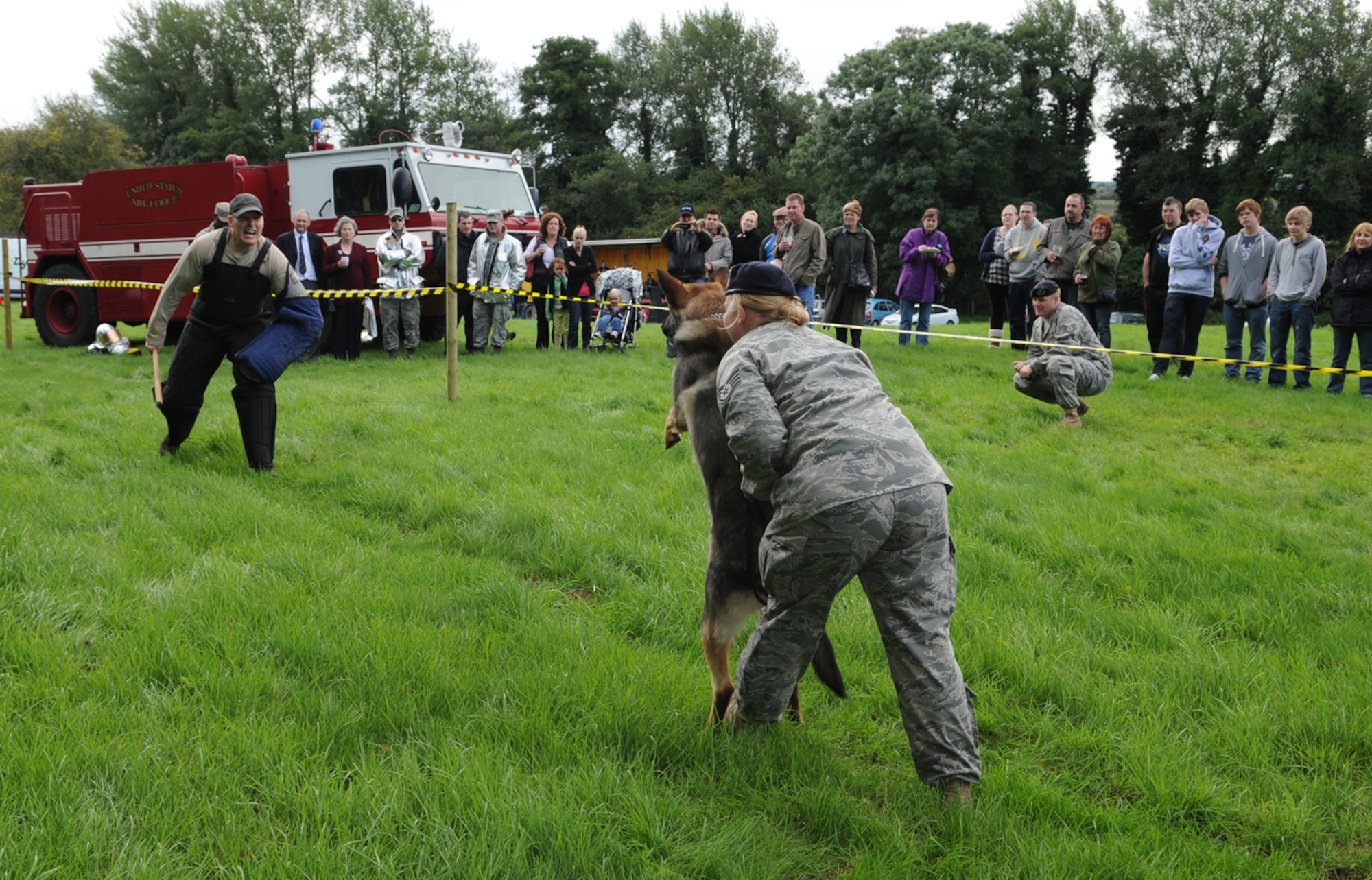 RAF MILDENHALL, England -- Staff Sgt. Grant Champeaux, 100th Security Forces Squadron, acts as an aggressor towards Military Working Dog Zulton, held back by handler Staff Sgt. Meredith Clement, during a working dog demonstration at an event in Icklingham, near Bury St. Edmunds, Aug. 29. The event was held in the local community to raise money for the East Anglian Air Ambulance and members from the 100th SFS MWD section and 100th Civil Engineer Squadron Fire Department supported this as one of many they attend in the local community throughout the year. Despite constant and heavy rain, which sent the crowd running for shelter before the demonstration, the RAF Mildenhall members braved the weather and showed their staunch support for the event by continuing with the demonstation and chatting with members of the public. (U.S. Air Force photo/Karen Abeyasekere)