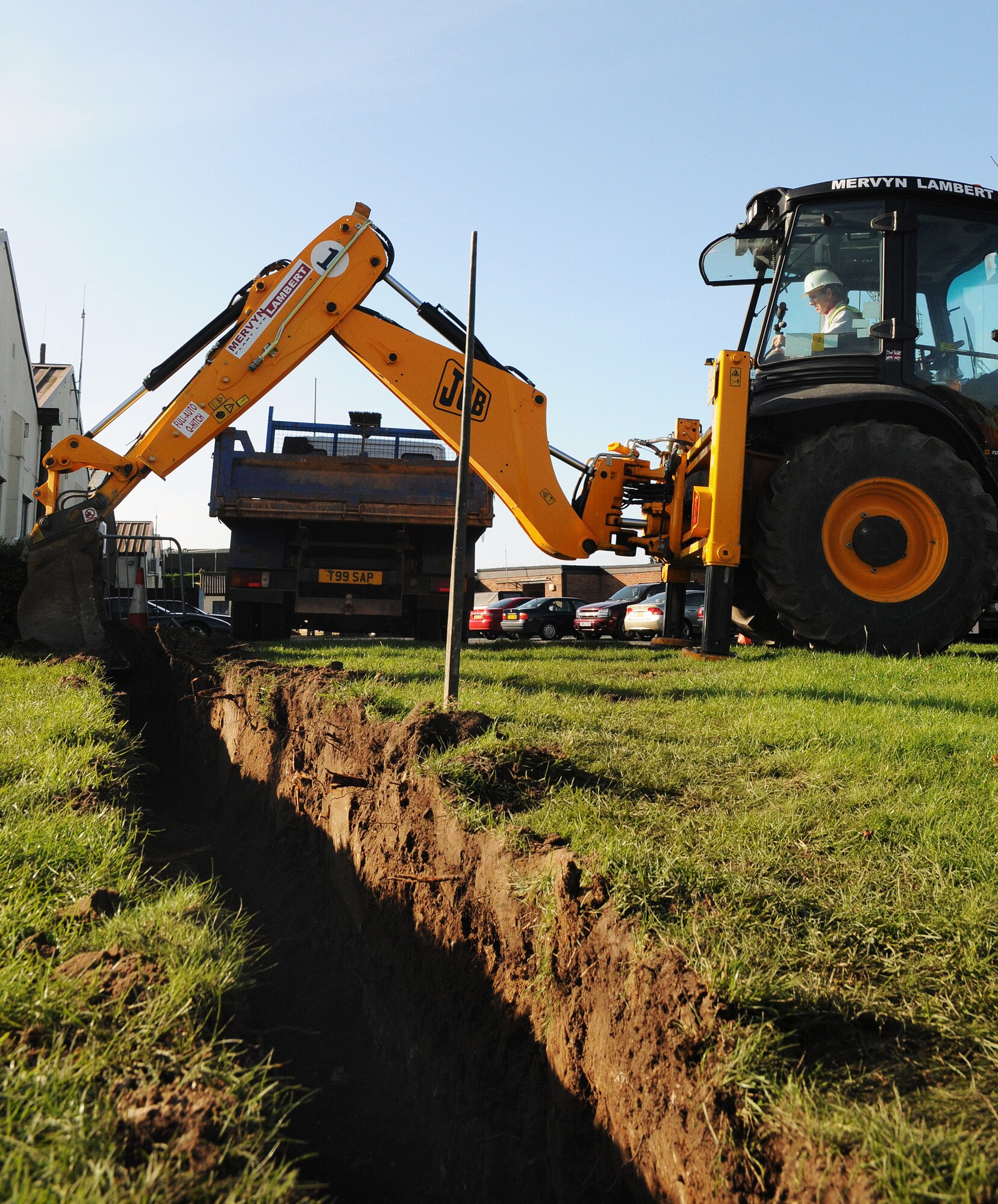 RAF MILDENHALL, England -- David Dodge, a local contractor, uses a digger to excavate a trench for installing security bollards here Aug. 31. As part of antiterrorism and force protection measures, the bollards are secured underground by a thick layer of concrete. Enough room is left, however for landscaping to grow over top the cement. (U.S. Air Force photo/Staff Sgt. Thomas Trower)