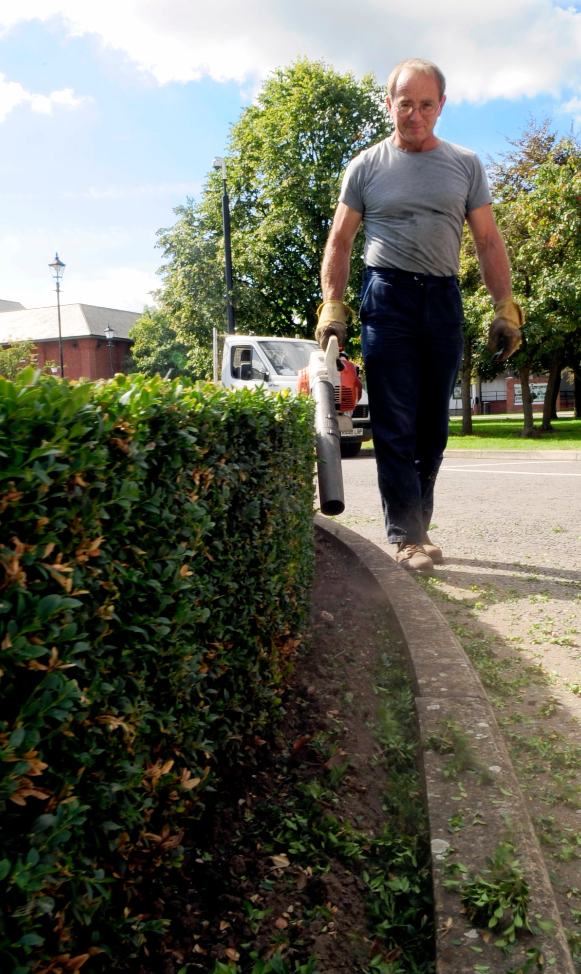 RAF MILDENHALL, England – Garry Brown, a local contractor, uses a blower to remove hedge trimmings out of the flowerbed around the flag poles in front of the wing headquarters building here Sept. 3. The contractors maintain the landscape on base year around. (U.S. Air Force photo/Senior Airman Ethan Morgan)