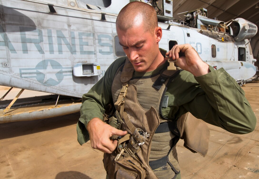 Lance Cpl. Jeffrey Wyman, a flight equipment technician with Marine Heavy Helicopter 361, 3rd Marine Aircraft Wing (Forward), puts flight equipment on over the new Micro Climate Cooling Unit System outside his squadron's hangar on the flight line here Sept. 4. The McCUS cirulates cold liquid around crew chiefs' and pilots' bodies during flight to reduce their core temperatures. The new vest raises energy levels and helps keep the crew and pilots focused while flying by keeping them cool during extended missions in high temperatures.
