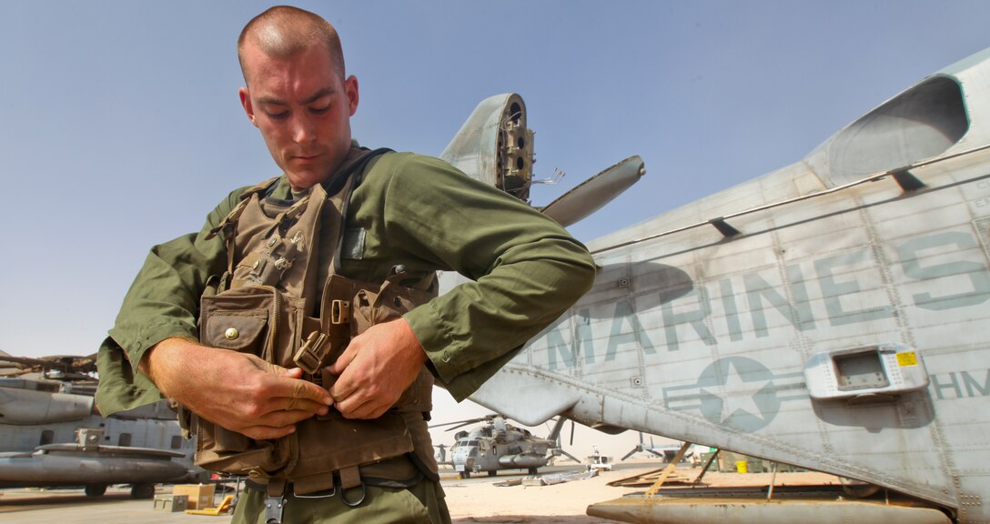 Lance Cpl. Jeffrey Wyman, a flight equipment technician with Marine Heavy Helicopter 361, 3rd Marine Aircraft Wing (Forward), puts flight equipment on over the new Micro Climate Cooling Unit System outside his squadron's hangar on the flight line here Sept. 4. The McCUS cirulates cold liquid around crew chiefs' and pilots' bodies during flight to reduce their core temperatures. The new vest raises energy levels and helps keep the crew and pilots cool and focused while flying during extended missions in hot weather.