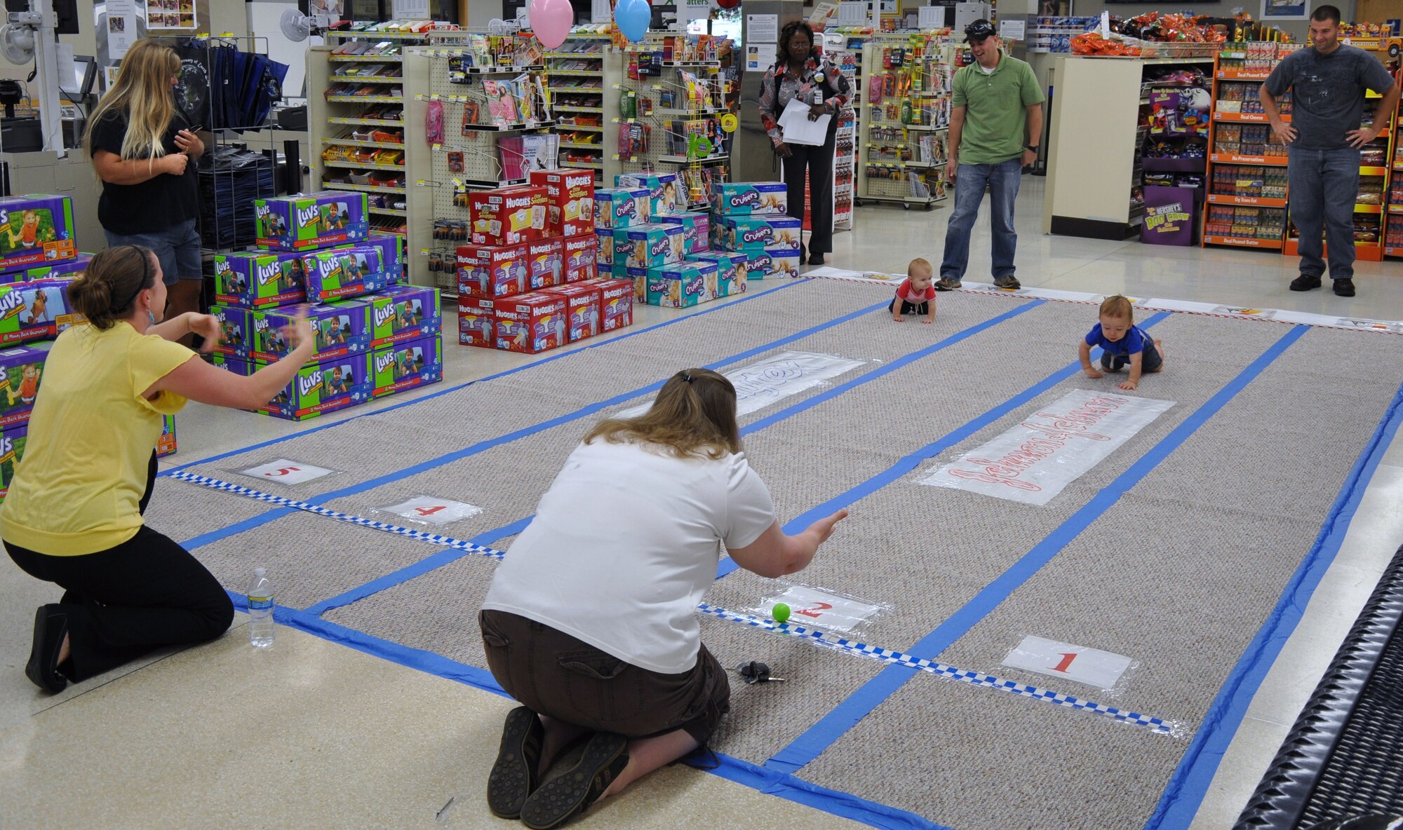 Alexis Chattin (left) urges her son Steven to speed to the finish line during the 10th Annual Hotter'n Heck Diaper Derby at the commissary on Sheppard Air Force Base, Texas, Sep. 5.  This year’s participants competed in a bracket-style race that ended with Ethan Neu (right), 11 months old, winning the grand prize pedal bike.  (U.S. Air Force photo/Tech. Sgt. Vernon Cunningham)