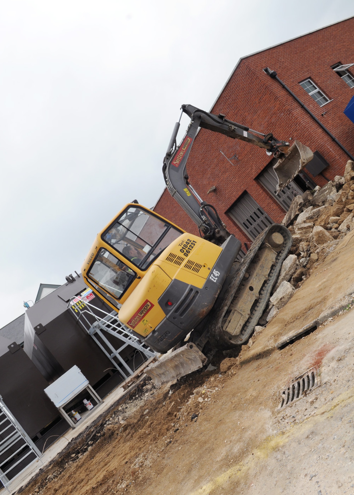 RAF MILDENHALL, England -- Jady Peachey, local contractor, uses a mini digger to move broken-up concrete Sept. 8, 2010 behind the Galaxy Club. The concrete is first broken up by pinning, then collected by the digger and transferred to a truck, before being taken off base for disposal. The area will then be re-concreted to make a slope for trucks to fill the nearby tanks. (U.S. Air Force photo/Karen Abeyasekere)