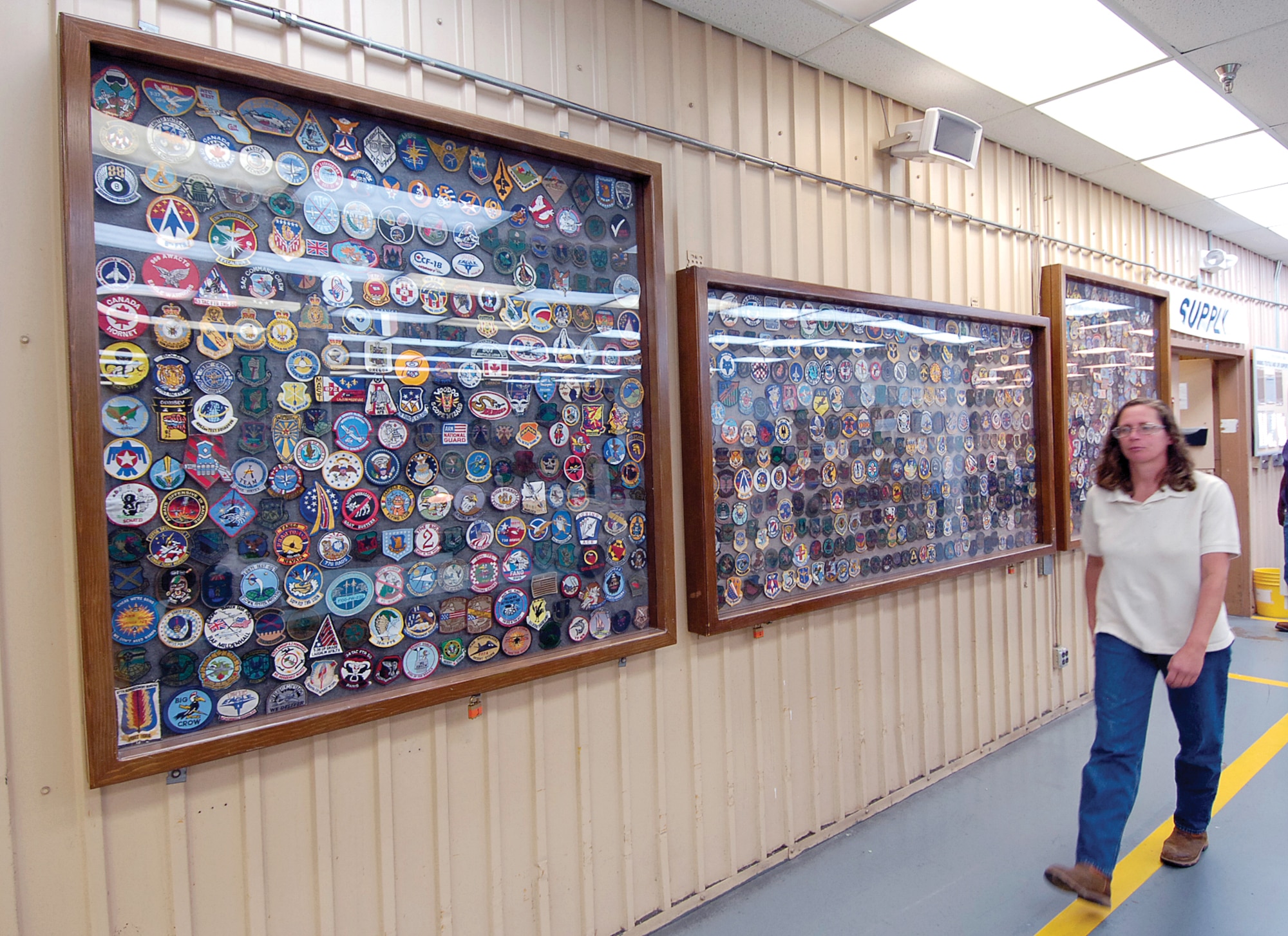 Fabric and Life Support Unit Chief Ann Jones passes hundreds of patches proudly displayed along a shop wall.  They come from every branch of service and squadrons all over the world who have used the unit’s services. (Air Force photo by Margo Wright) 