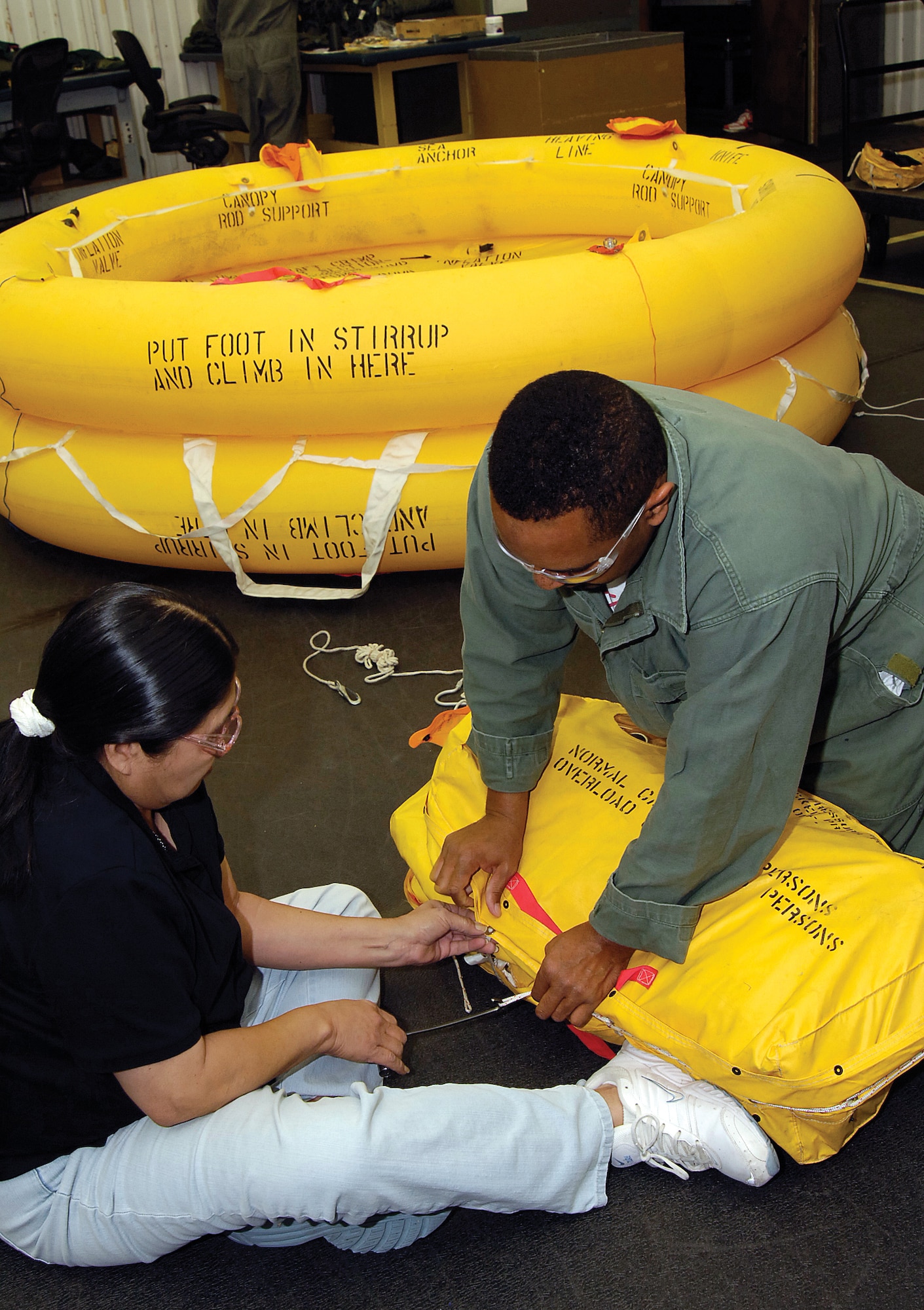 Donovan Peoples and Janice Lena repack a Navy 10-man life raft in the Textile and Life Support Unit located in Bldg. 229. Worker turnover in the unit is uncommon; many have more than 20 years of service and knowledge behind them. Ms. Lena, a training leader, has been with the shop for 33 years. (Air Force photo by Margo Wright) 