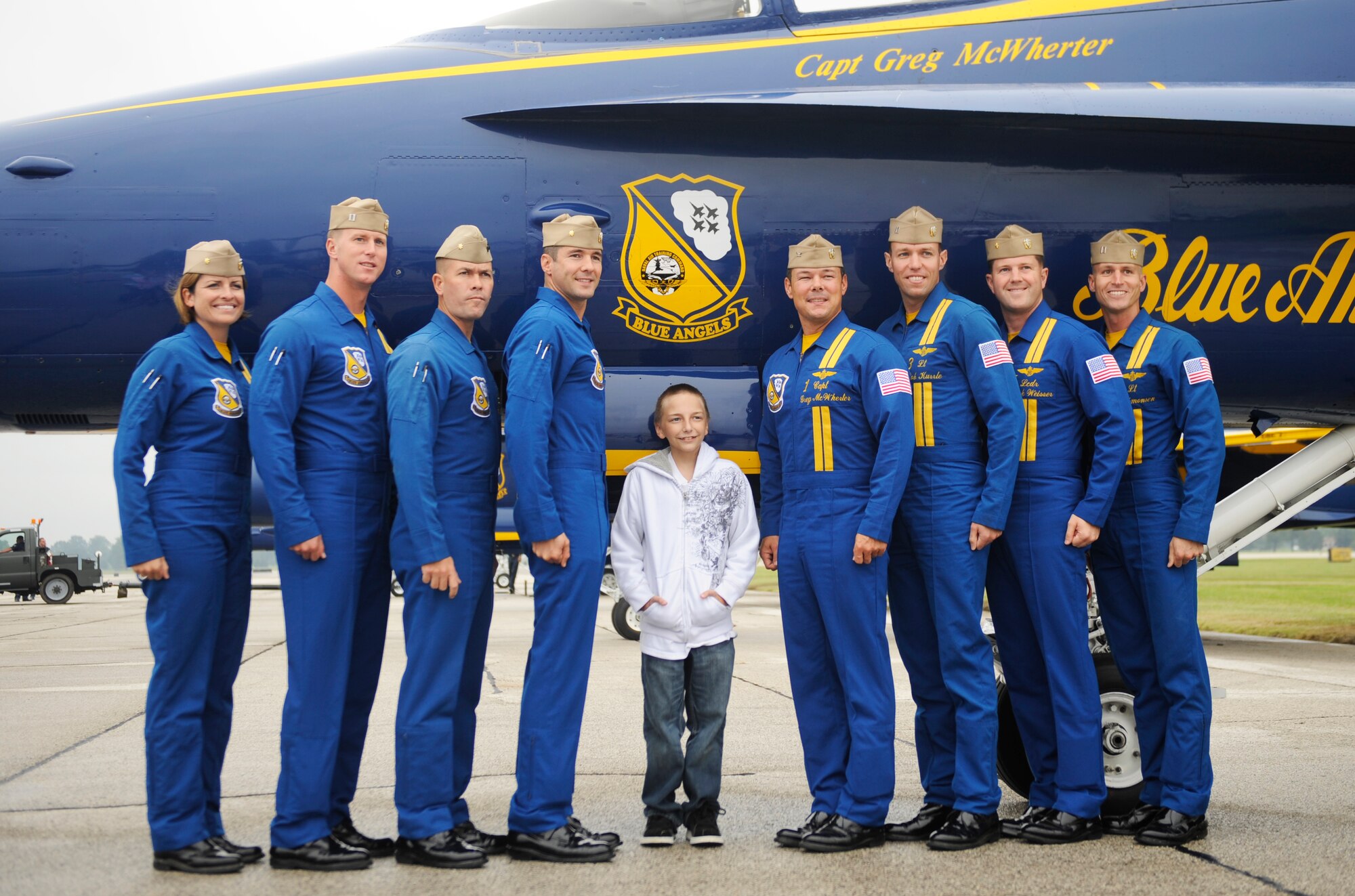 SCOTT AIR FORCE BASE, Ill. -- Jordan Krantz, whose wish as a part of the Make-A-Wish program was to meet a pilot, poses for a photo with the Blue Angels team in front of one of their planes Sept. 10 during the preview air show. The preview air show catered to the elderly and those with special needs. While the flying portion of the show was canceled due to inclement weather, attendees were able to tour static aircraft, talk with pilots and crew and bounce houses were available for children. (U.S. Air Force photo/Staff Sgt. Ryan Crane)